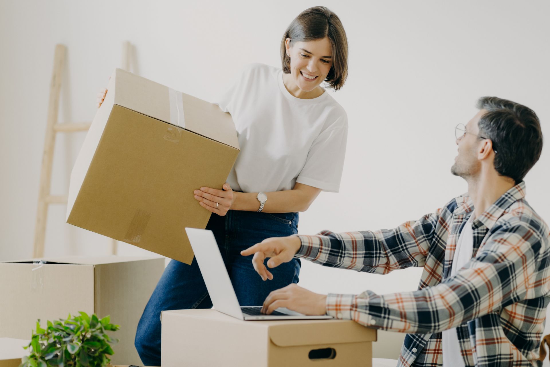 A woman is holding a cardboard box while a man is using a laptop.