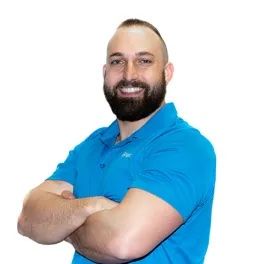 a man with a beard is wearing a blue shirt and smiling with his arms crossed .