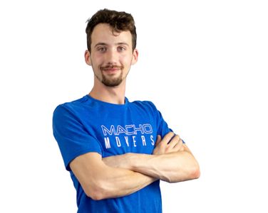 a man wearing a blue shirt that says macho movers is standing with his arms crossed .