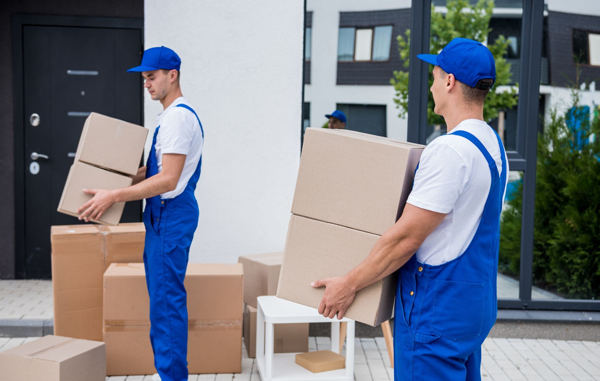 Two men are carrying boxes and a chair in front of a house.