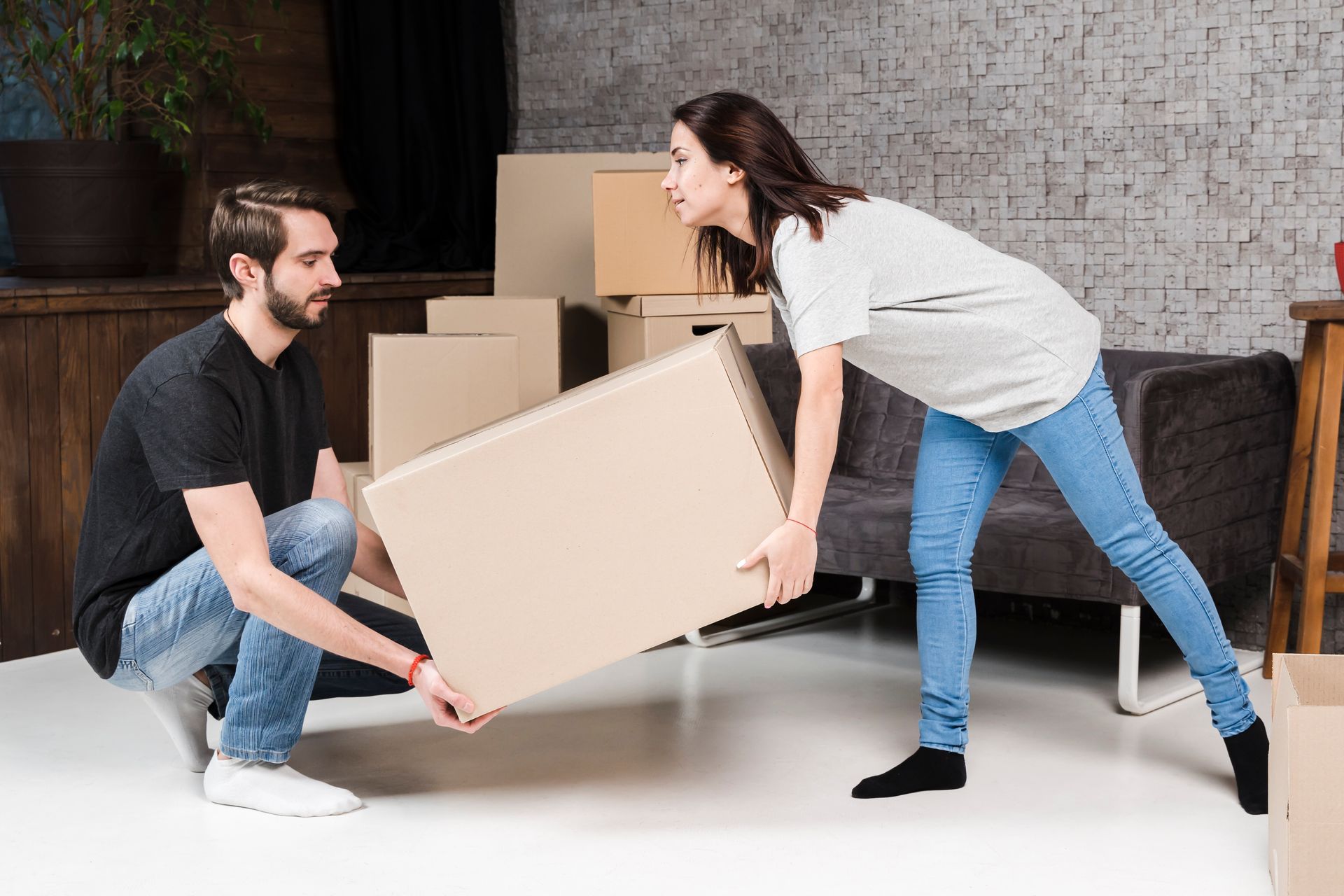 A man and a woman are carrying a cardboard box in a living room.