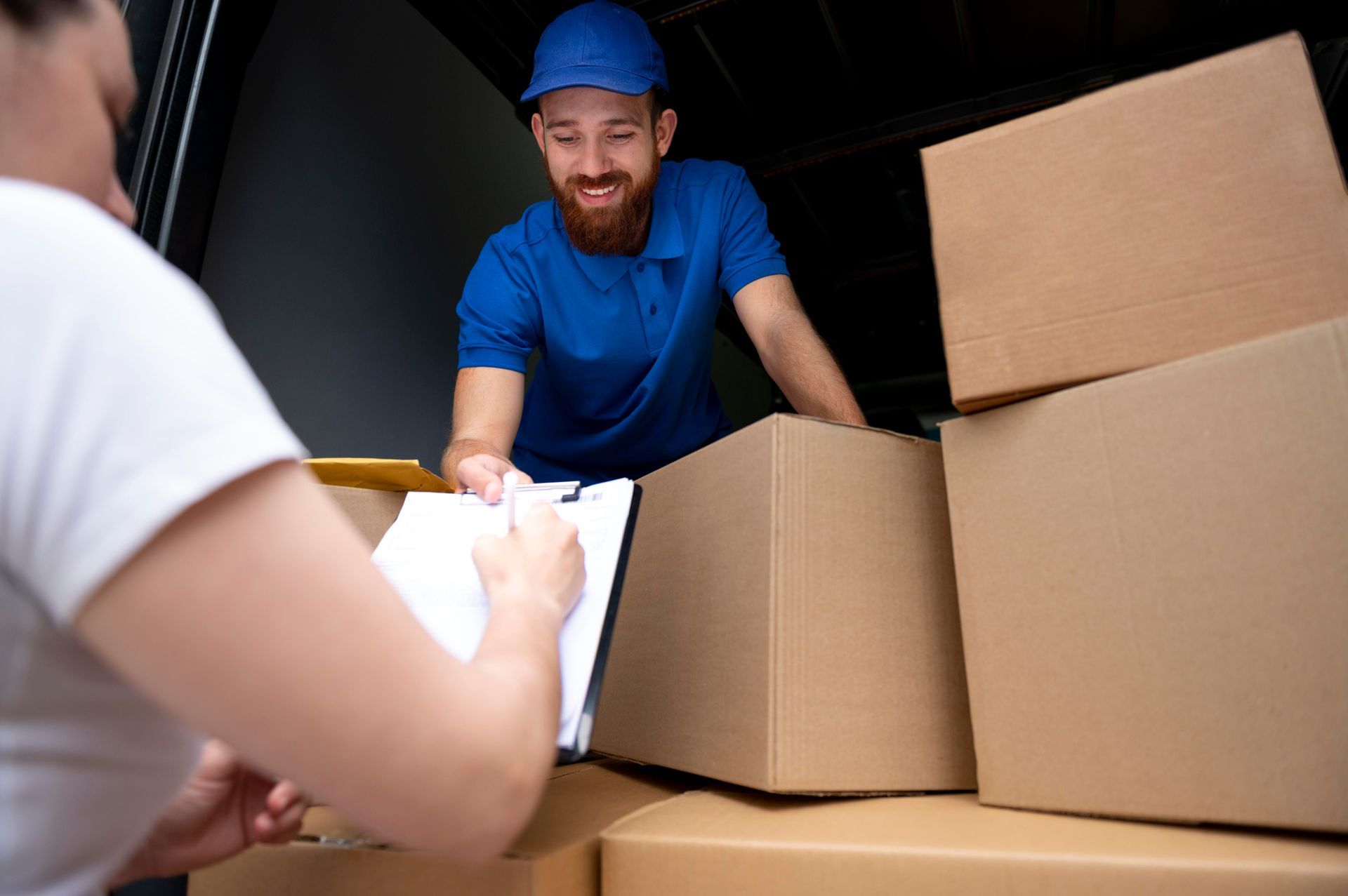 a delivery man is loading boxes into a truck while a woman writes on a clipboard.