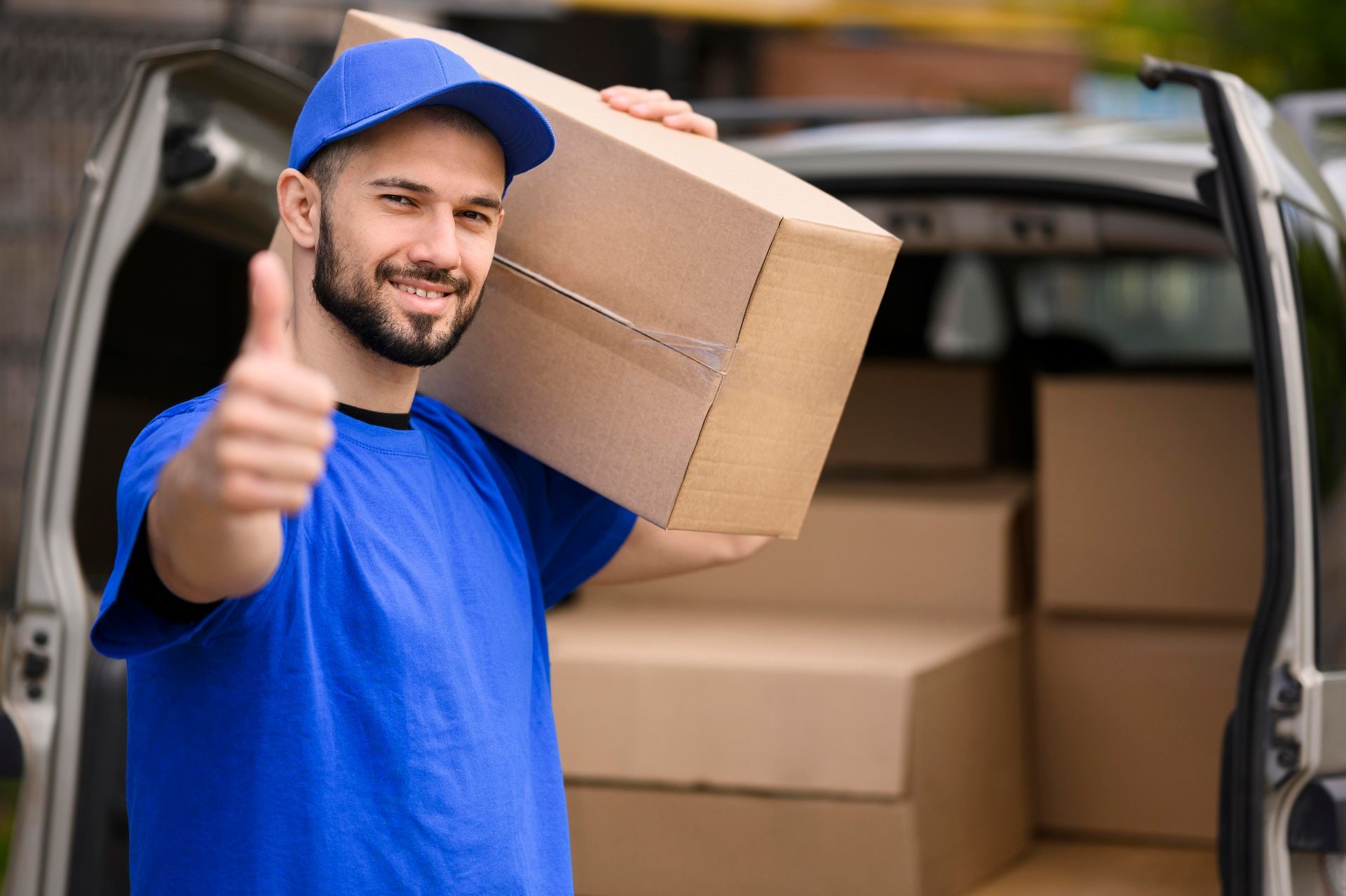 a delivery man is holding a cardboard box and giving a thumbs up .