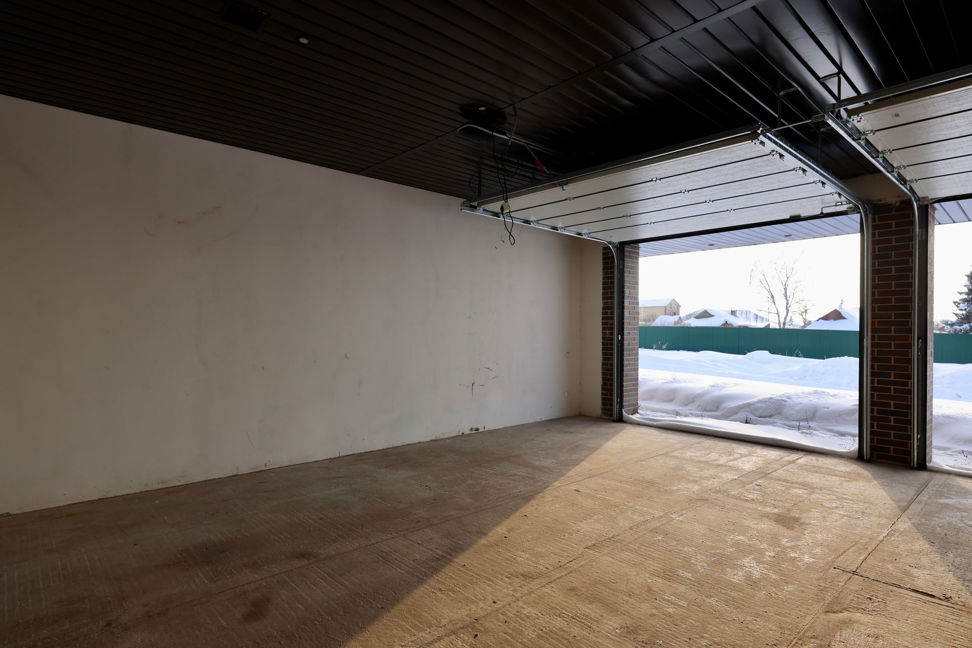 An empty garage with a garage door open and a view of the snow outside.