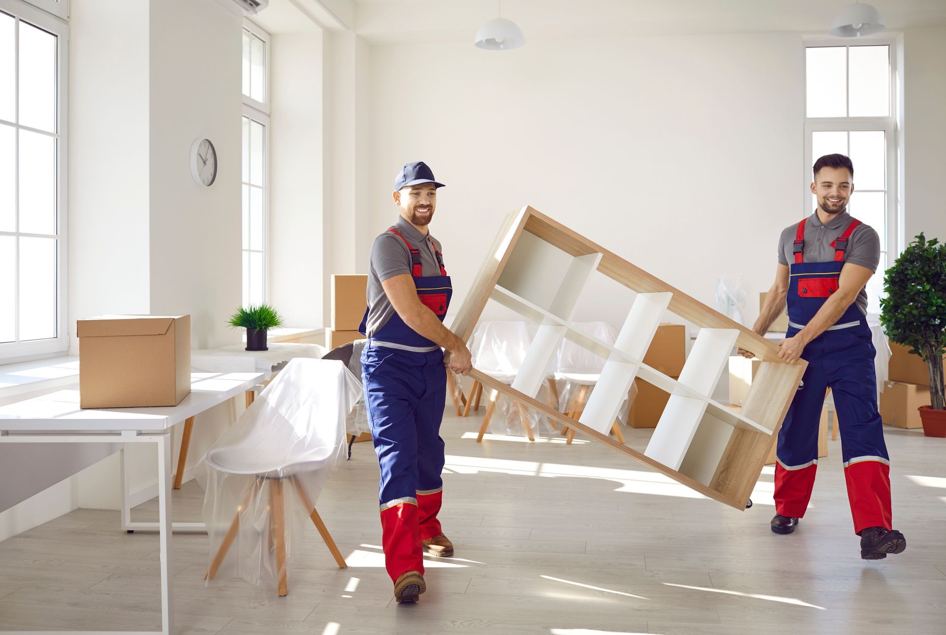 two men are carrying a couch wrapped in plastic in a living room .