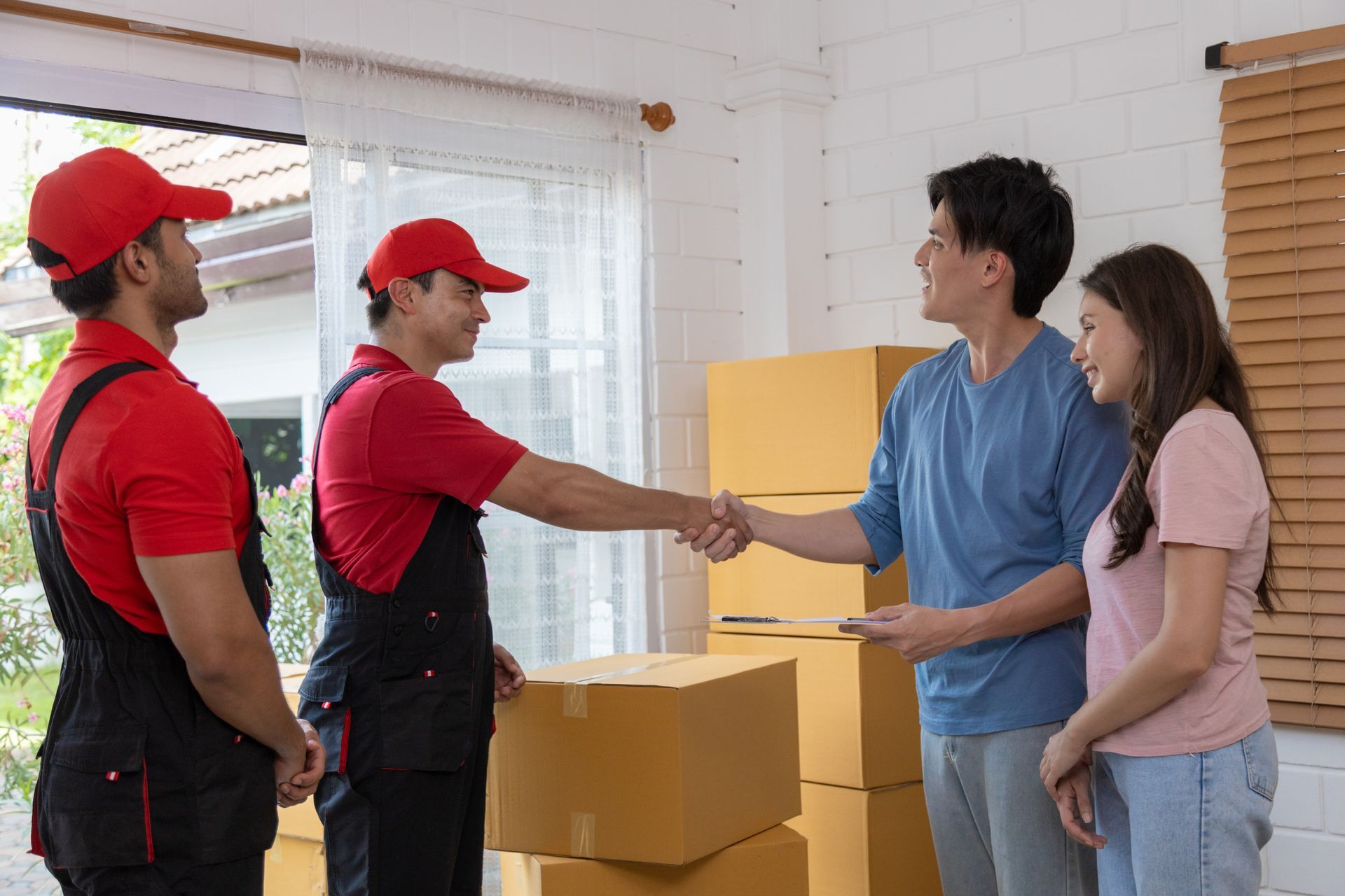 A group of movers are shaking hands with a family in a living room.