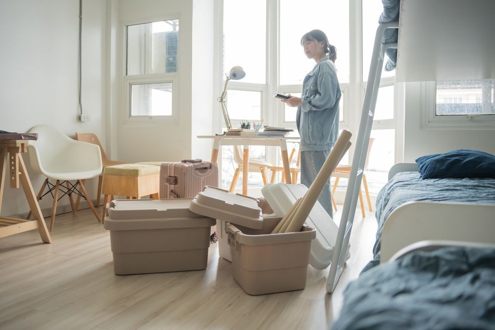 A woman is standing in a room filled with boxes and looking at her phone.