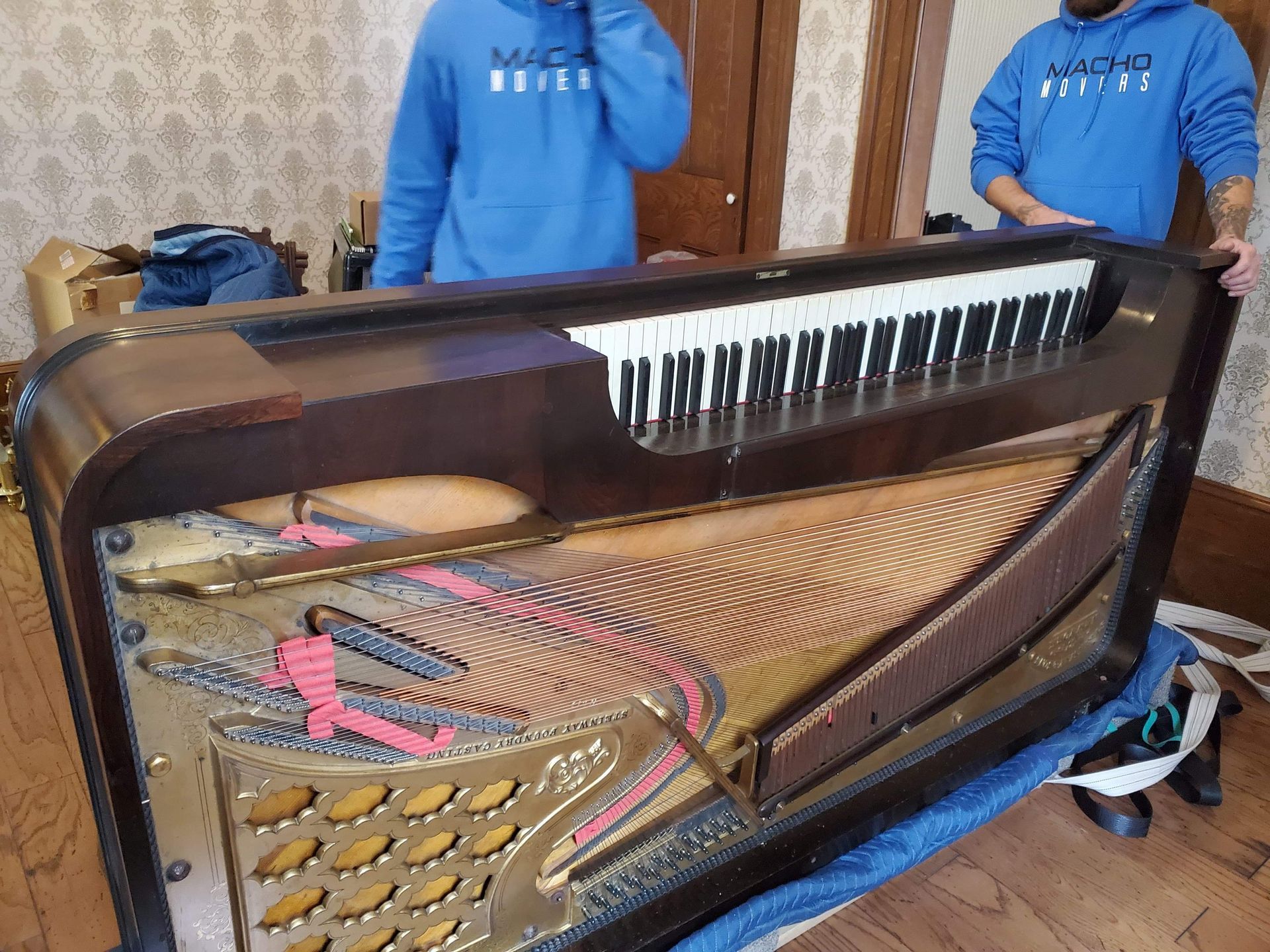 A man in a blue hoodie is standing next to a piano