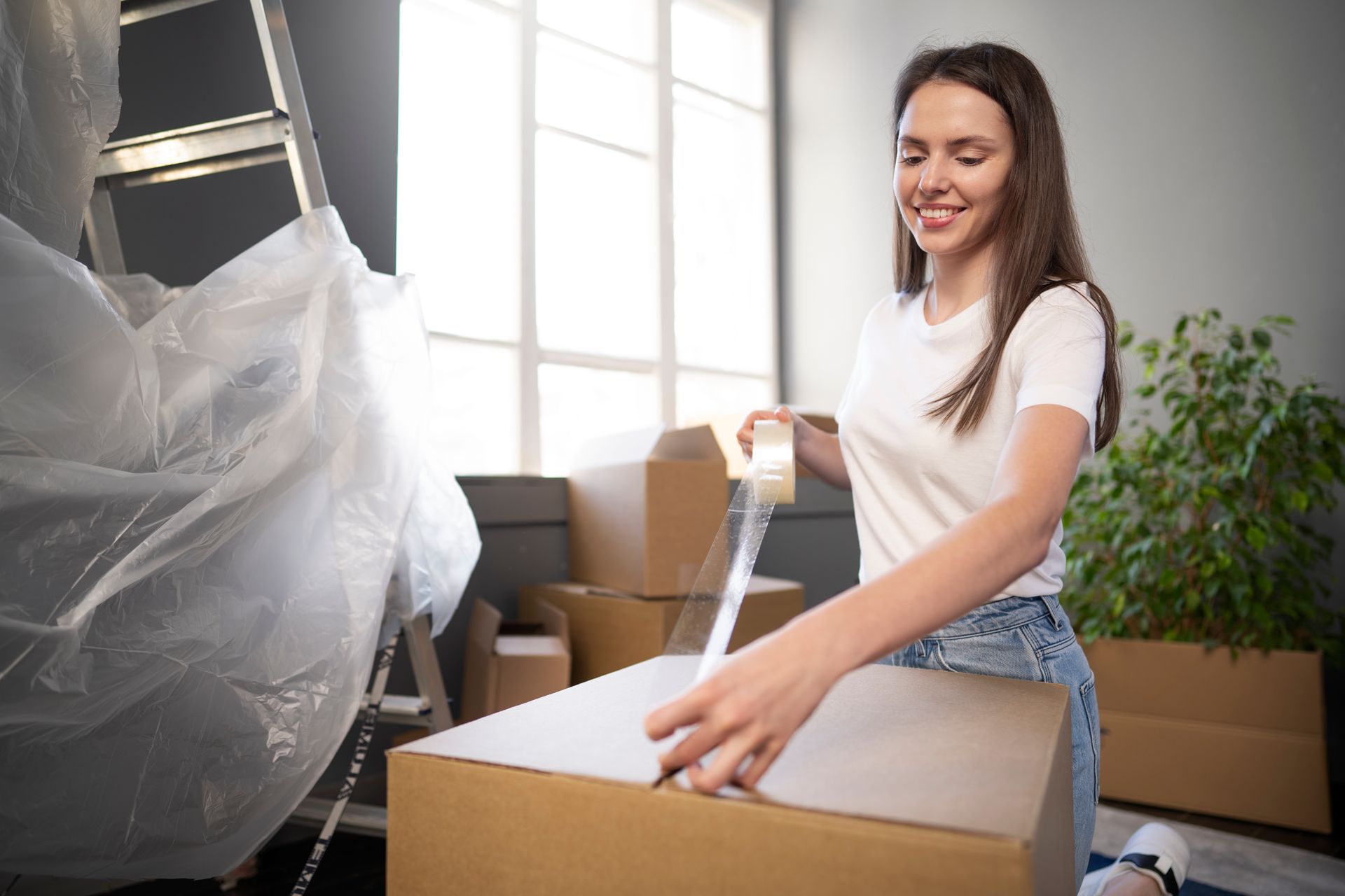 A woman is wrapping a cardboard box with tape.