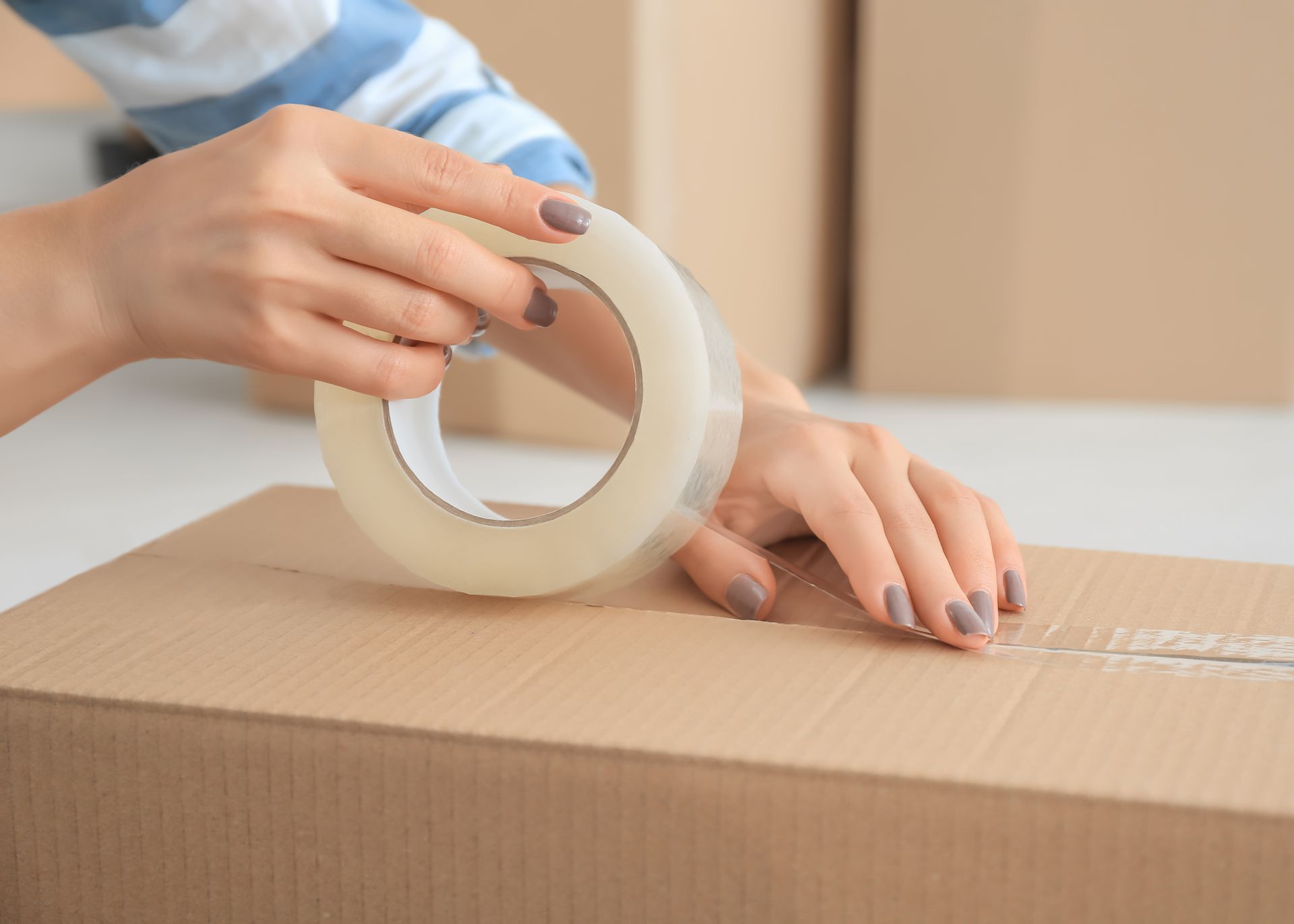 A woman is taping a cardboard box with tape.