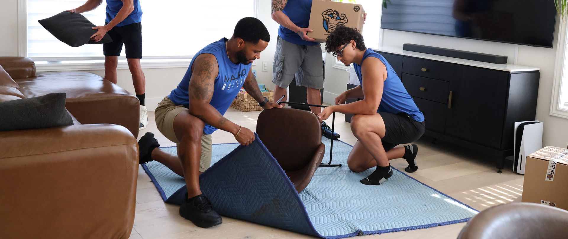 Movers wrapping a chair in a protective blanket, inside a living room.