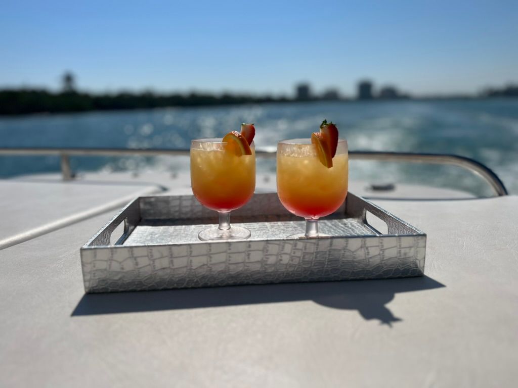Two cocktails in glasses on a tray on a boat with water and a skyline in the background.