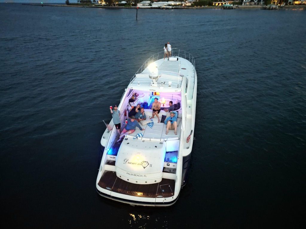 Boat at night with people, lit up, on water near a town.