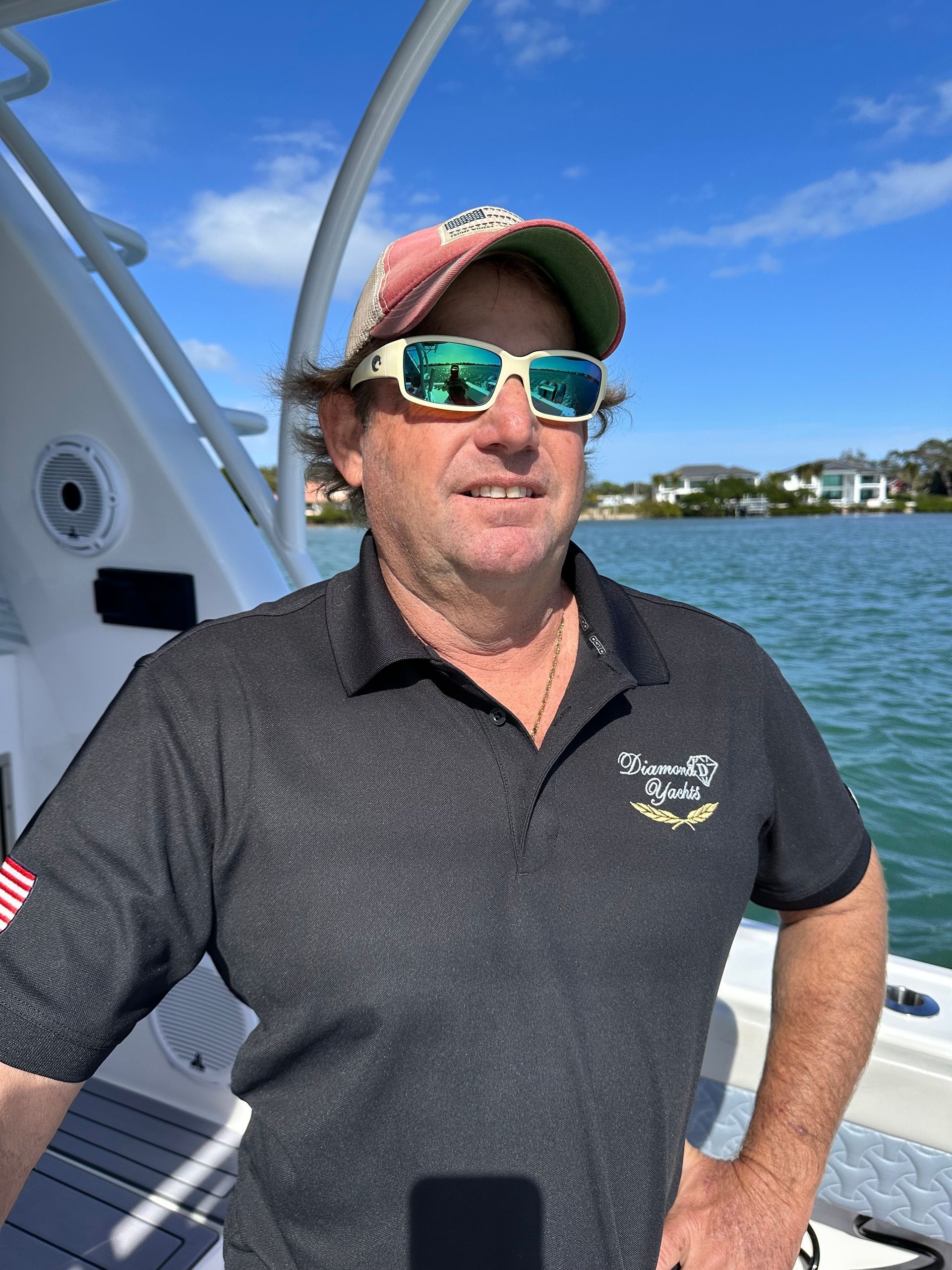 Man in sunglasses on a boat, wearing a hat and black polo shirt, outdoors.
