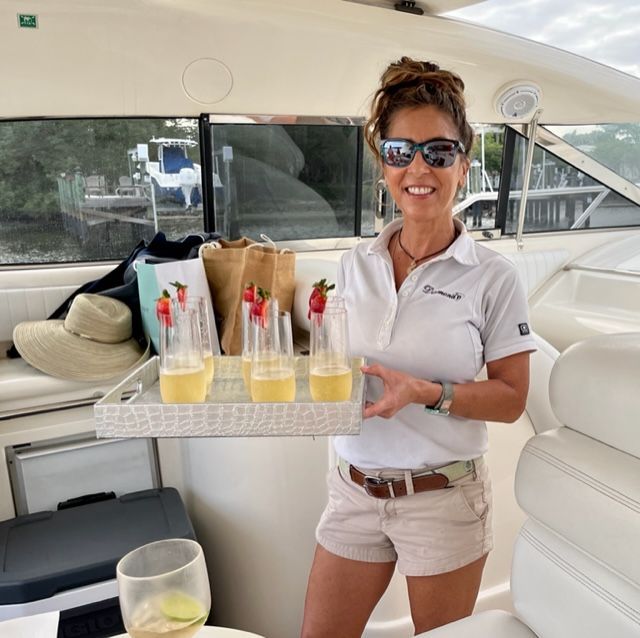 Woman on a boat smiles, holding a tray of drinks with strawberries; sunny day.