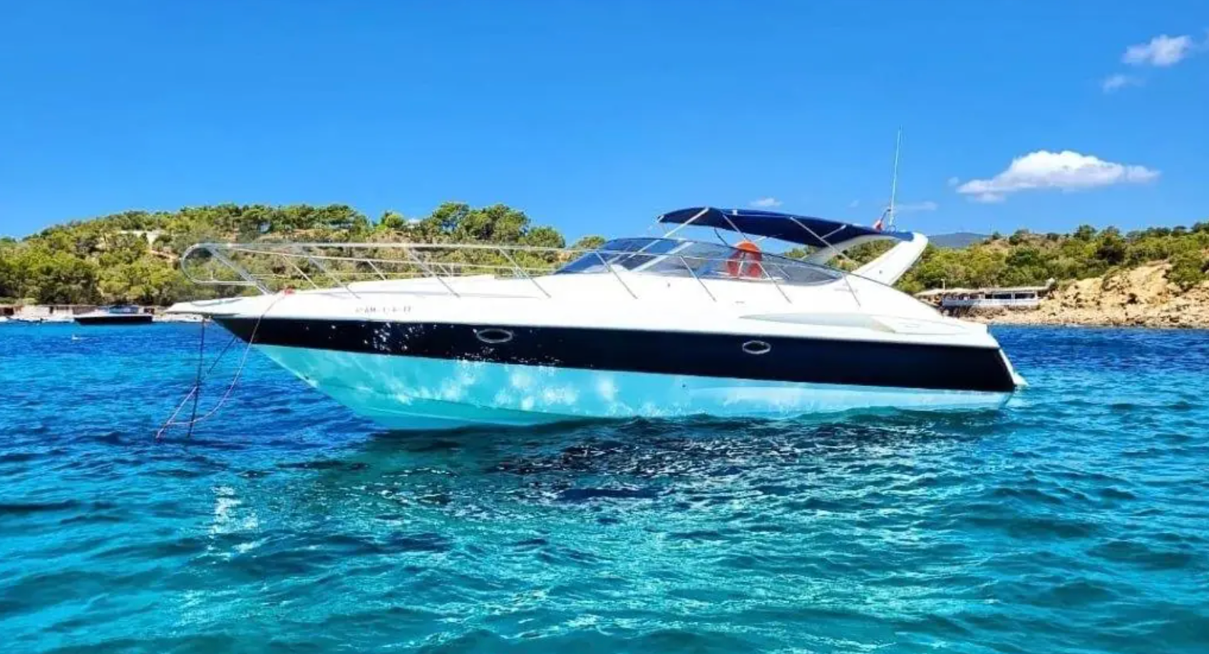 White motorboat on blue water near a coastline, under a bright, clear sky.