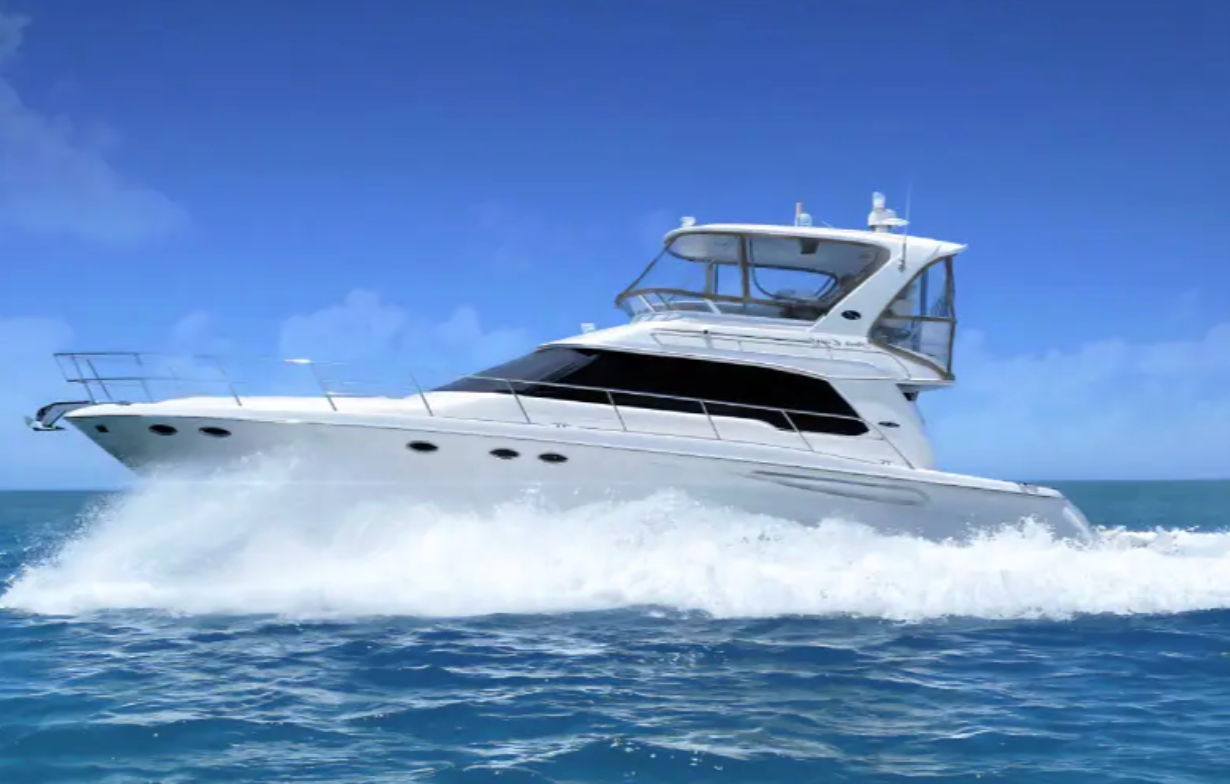 White yacht sailing across blue ocean, creating a white wake under a bright blue sky.