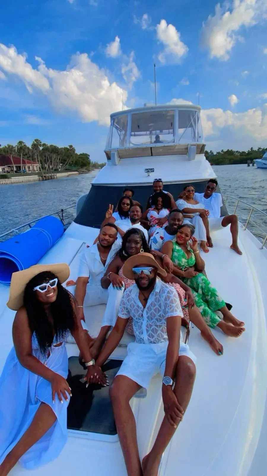 Group of people on a white boat, smiling. Clear sky with fluffy clouds.