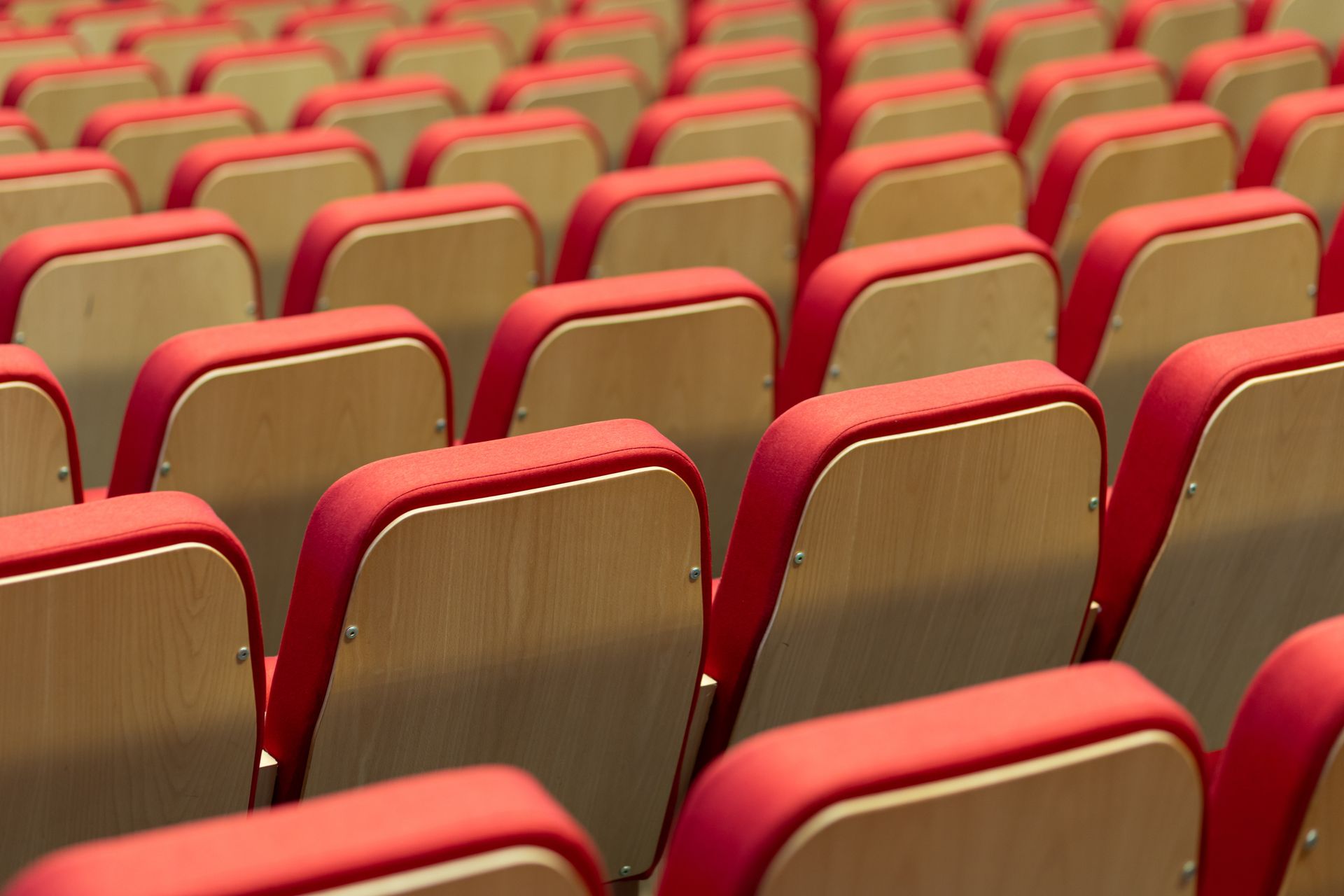 Rows of red seats in an auditorium with wooden arm rests.