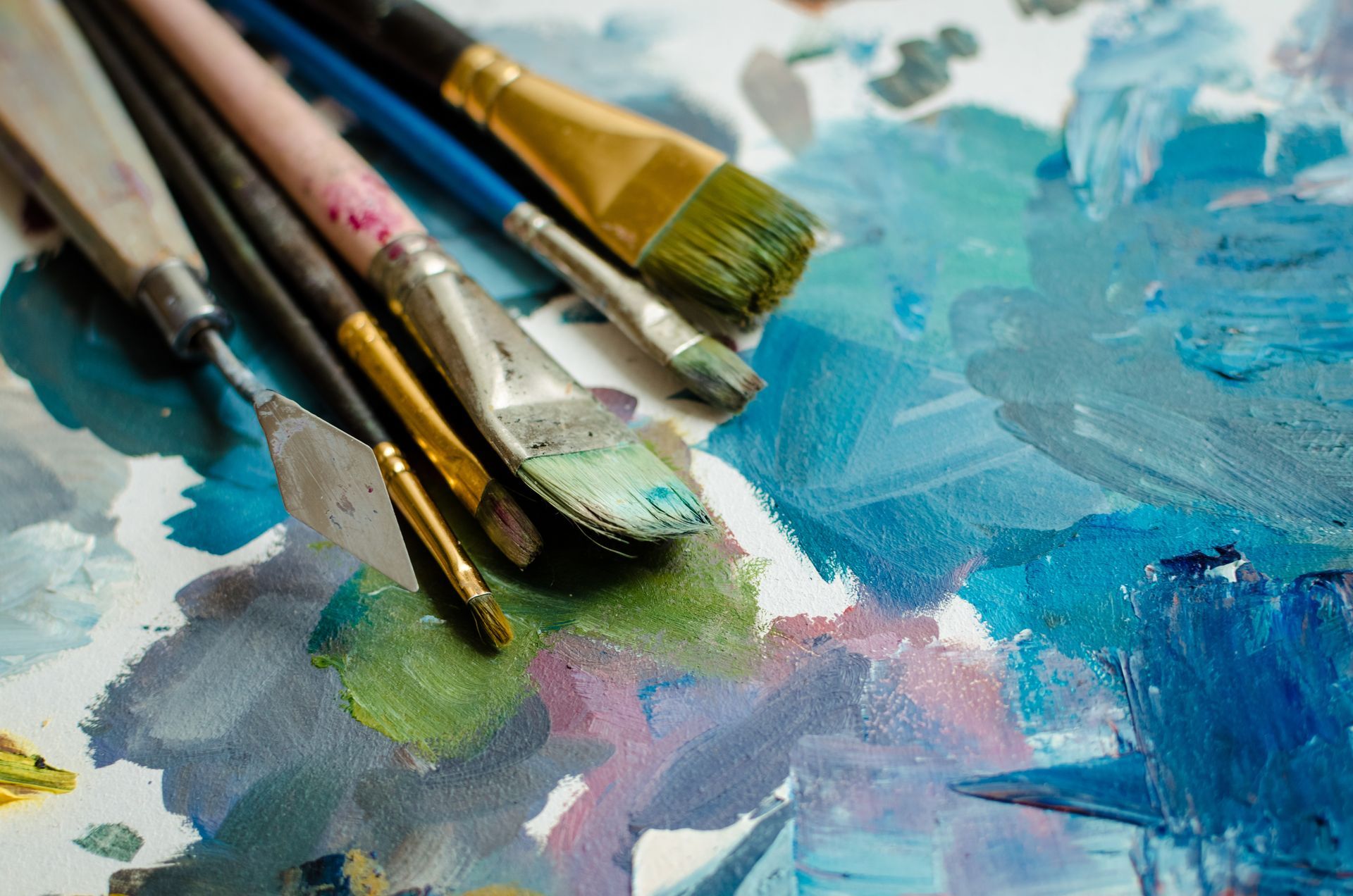 Paintbrushes and tubes of paint on a palette of blue and green paint.