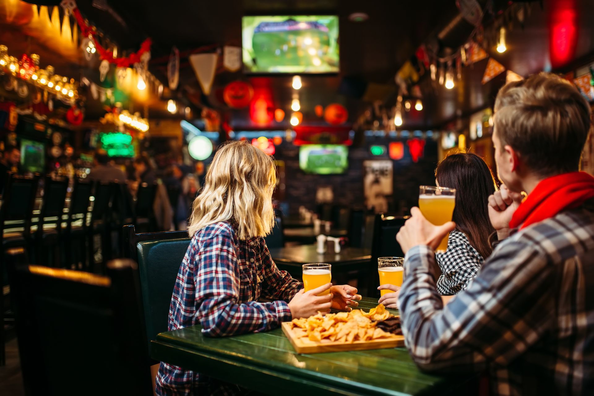 A group of people are sitting at a table in a bar drinking beer and watching a soccer game.