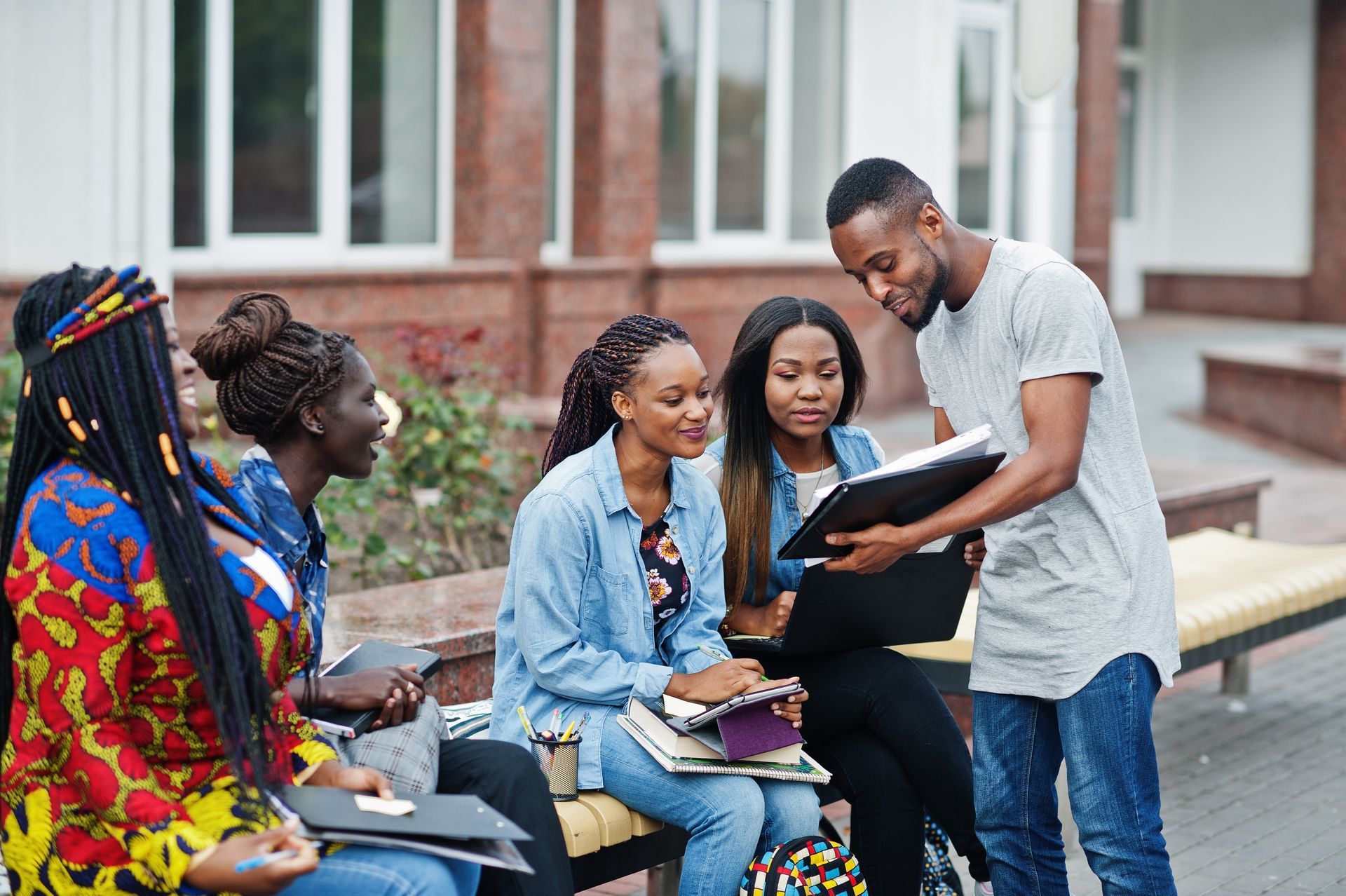 Students studying outdoors, looking at a folder. One person is holding the folder, explaining the contents to the group.