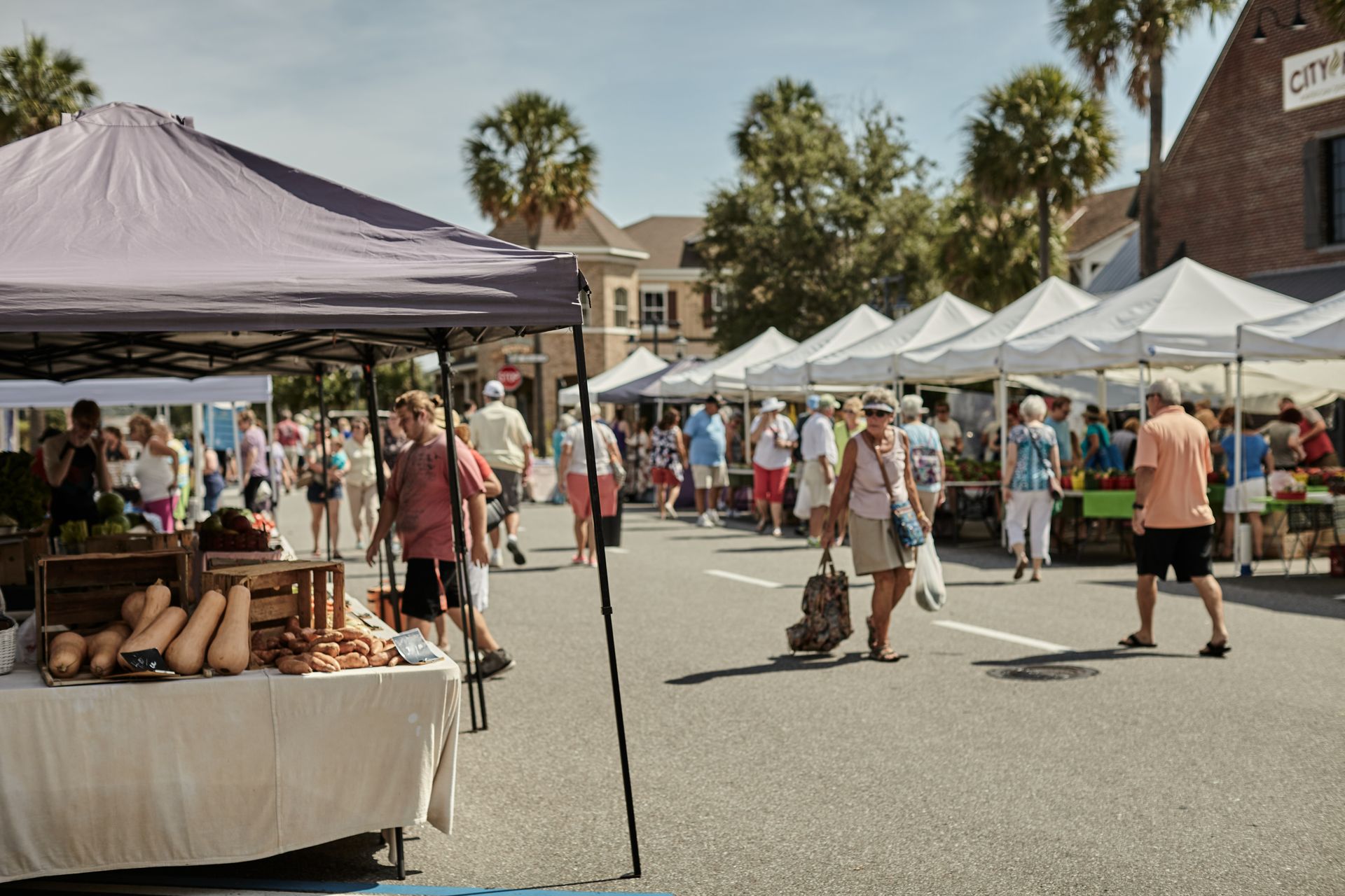 A group of people are walking down a street at a farmer 's market.