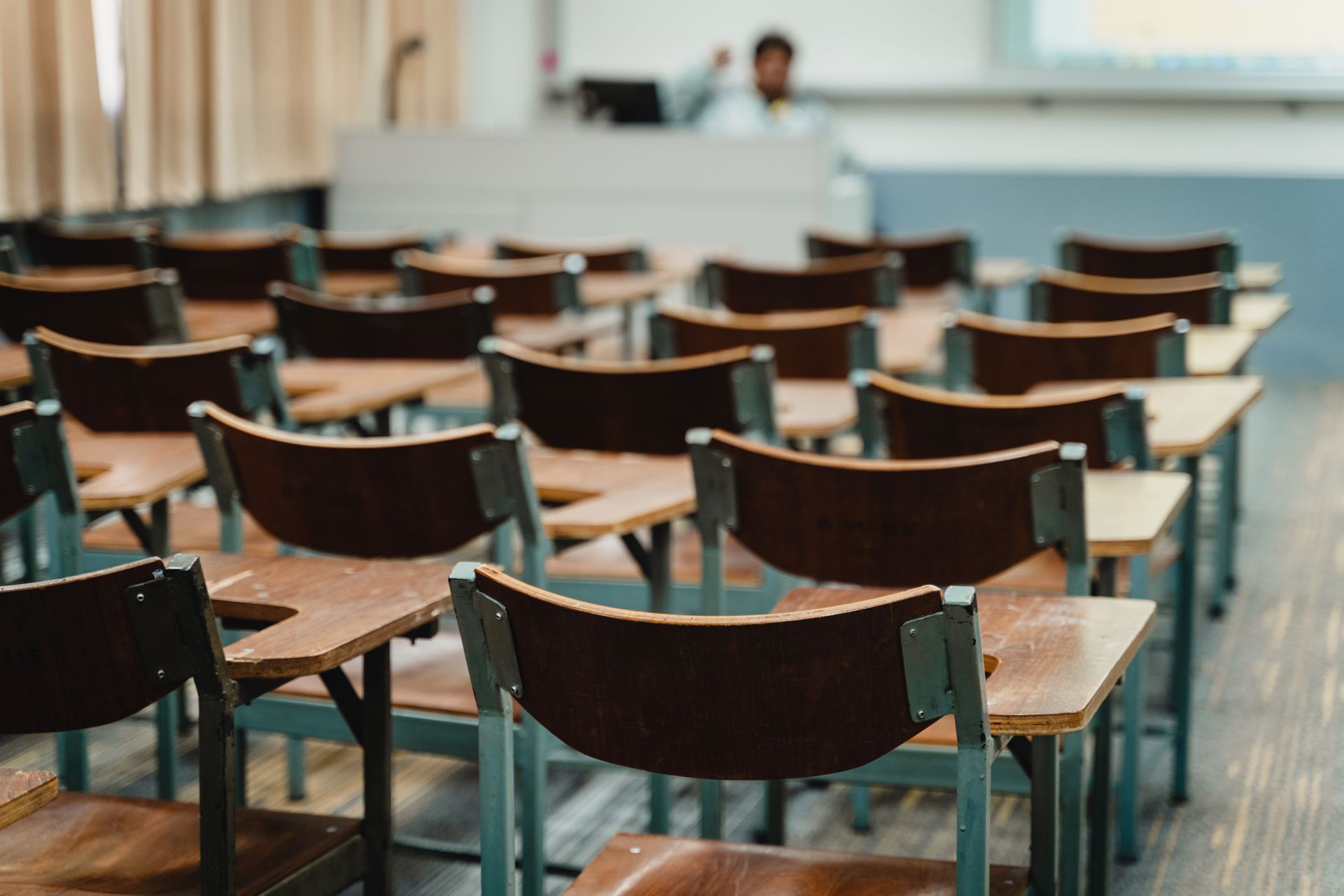 A row of wooden desks and chairs in a classroom.