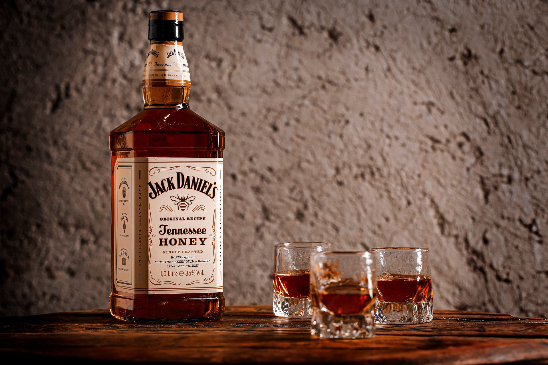 A bottle of jack daniels honey whiskey and two shot glasses on a wooden table.