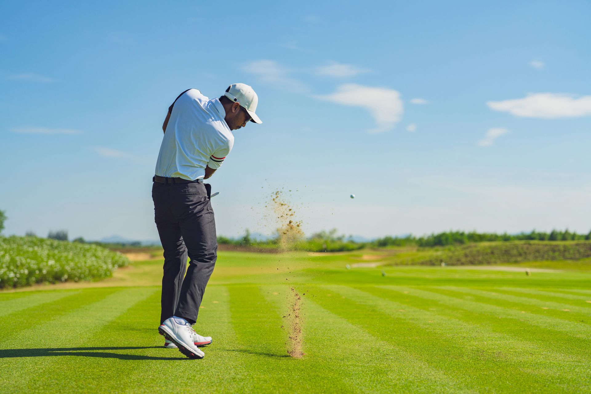 A man is swinging a golf club at a golf ball on a golf course.