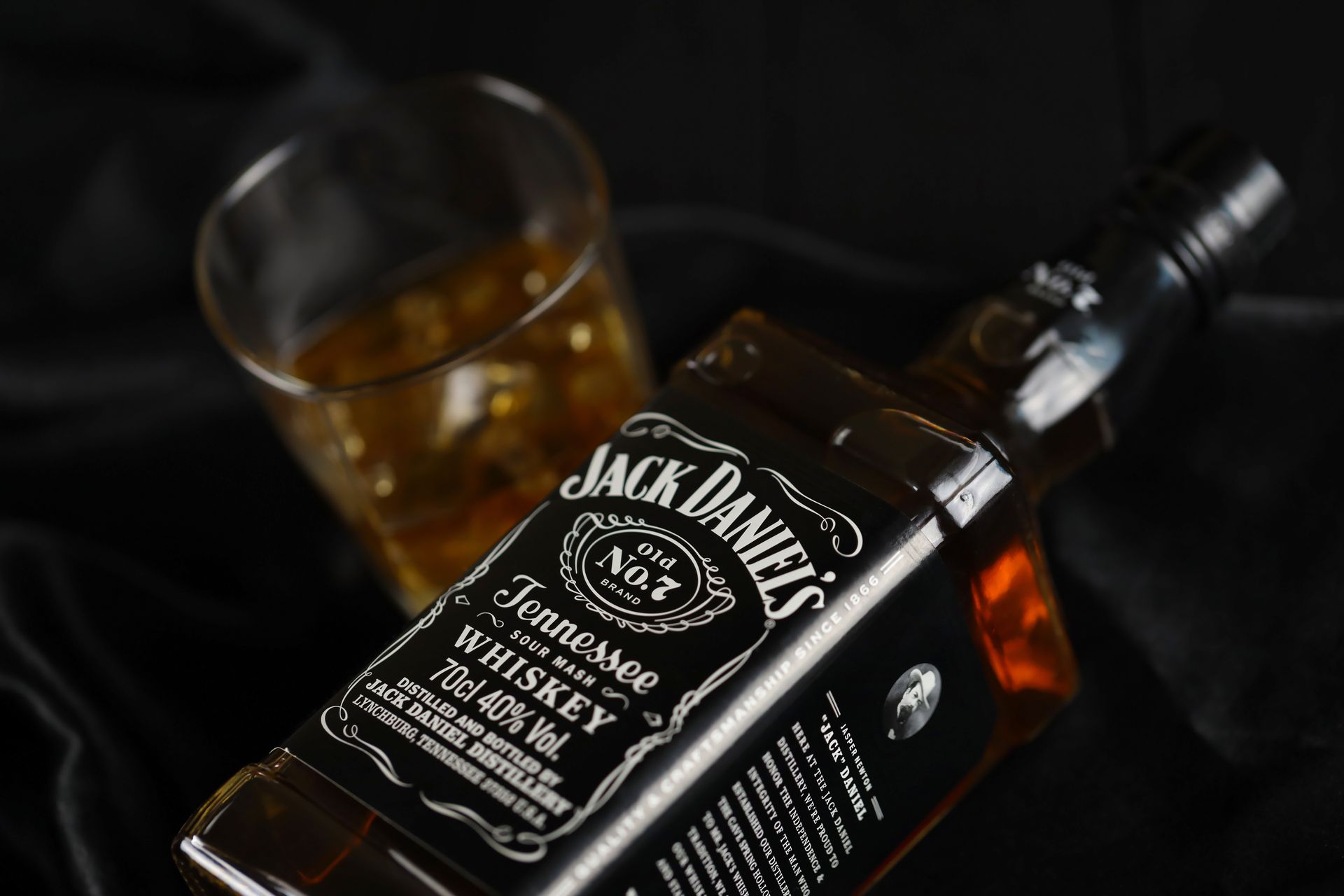 Jack Daniel's whiskey bottle and glass, amber liquid, on black fabric.