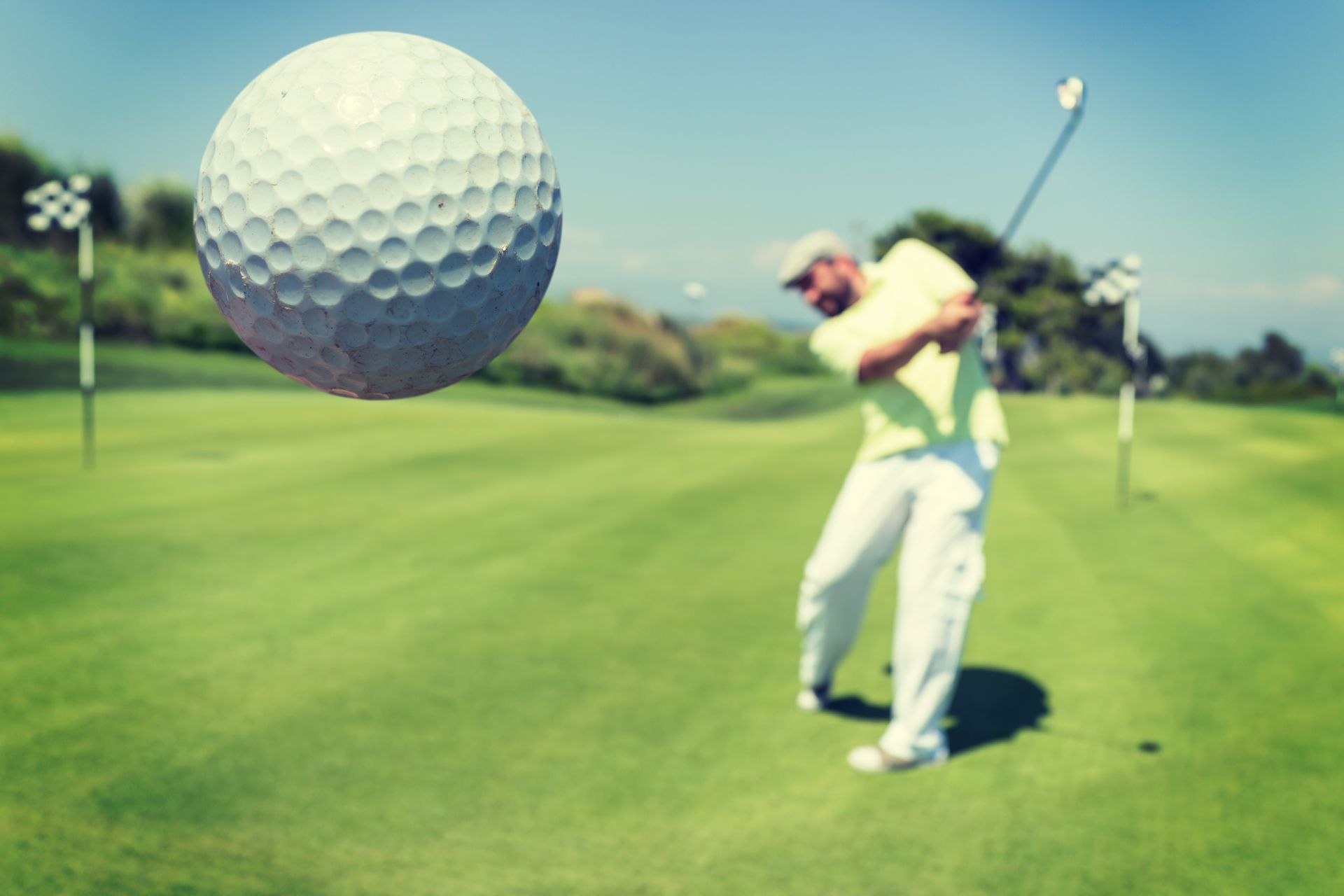 A man is swinging a golf club at a golf ball on a golf course.