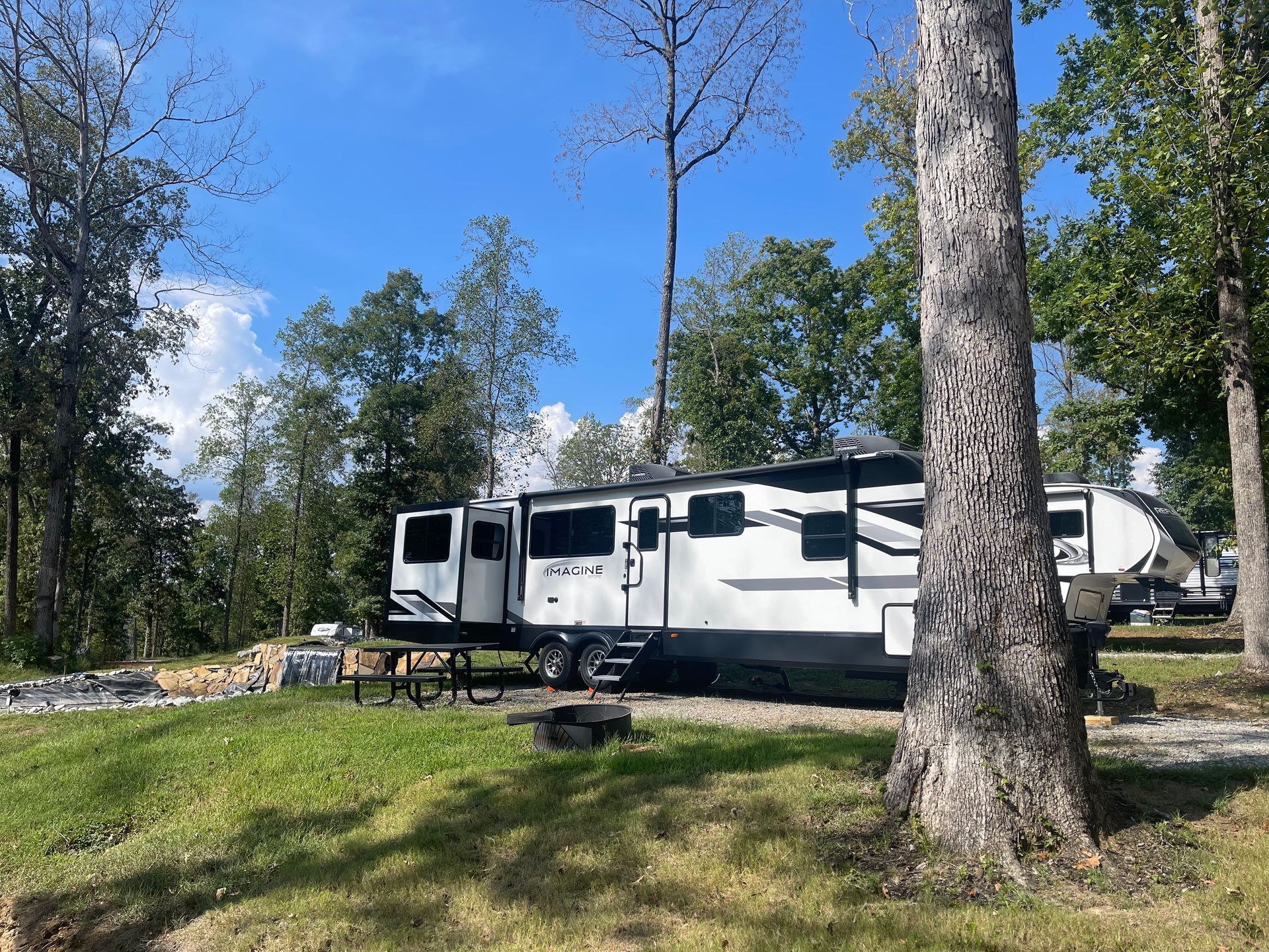 A white rv is parked in a grassy area surrounded by trees.