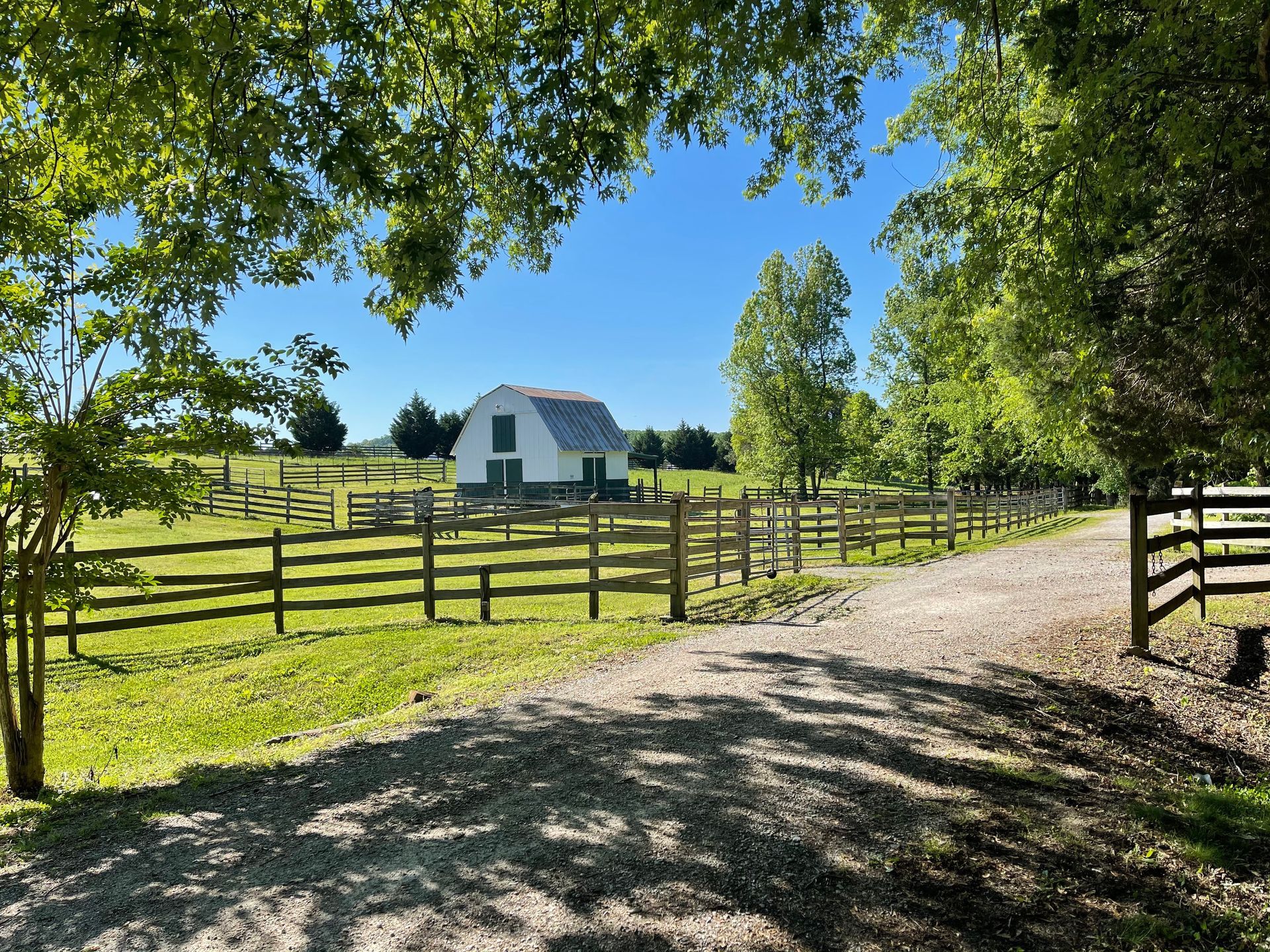 A white barn is surrounded by a wooden fence and a dirt road.