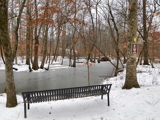 Waterside view of the a resting bench along the 1. 5 walking trail by the waterway during a winter snow fall