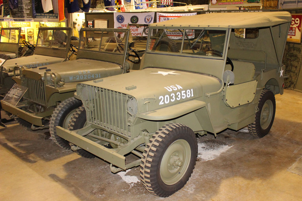 A row of old military jeeps are parked next to each other in a garage.