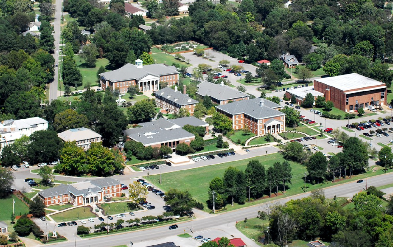 Aerial view of a college campus with several brick buildings, parking lots, and green spaces.