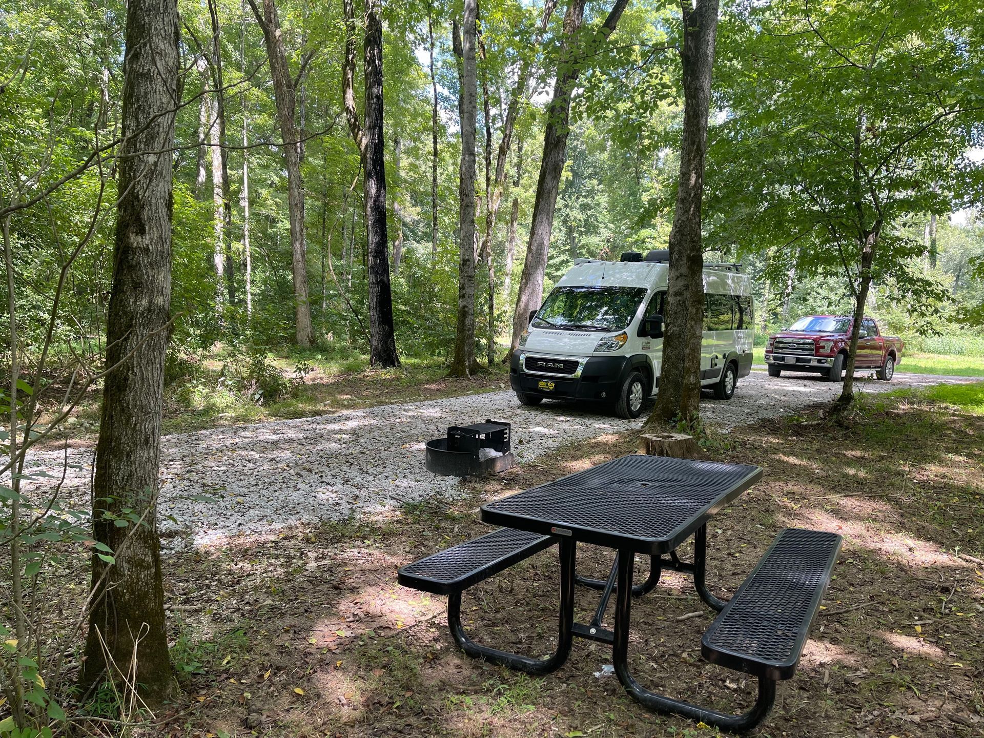 A white van is parked next to a picnic table in the woods.