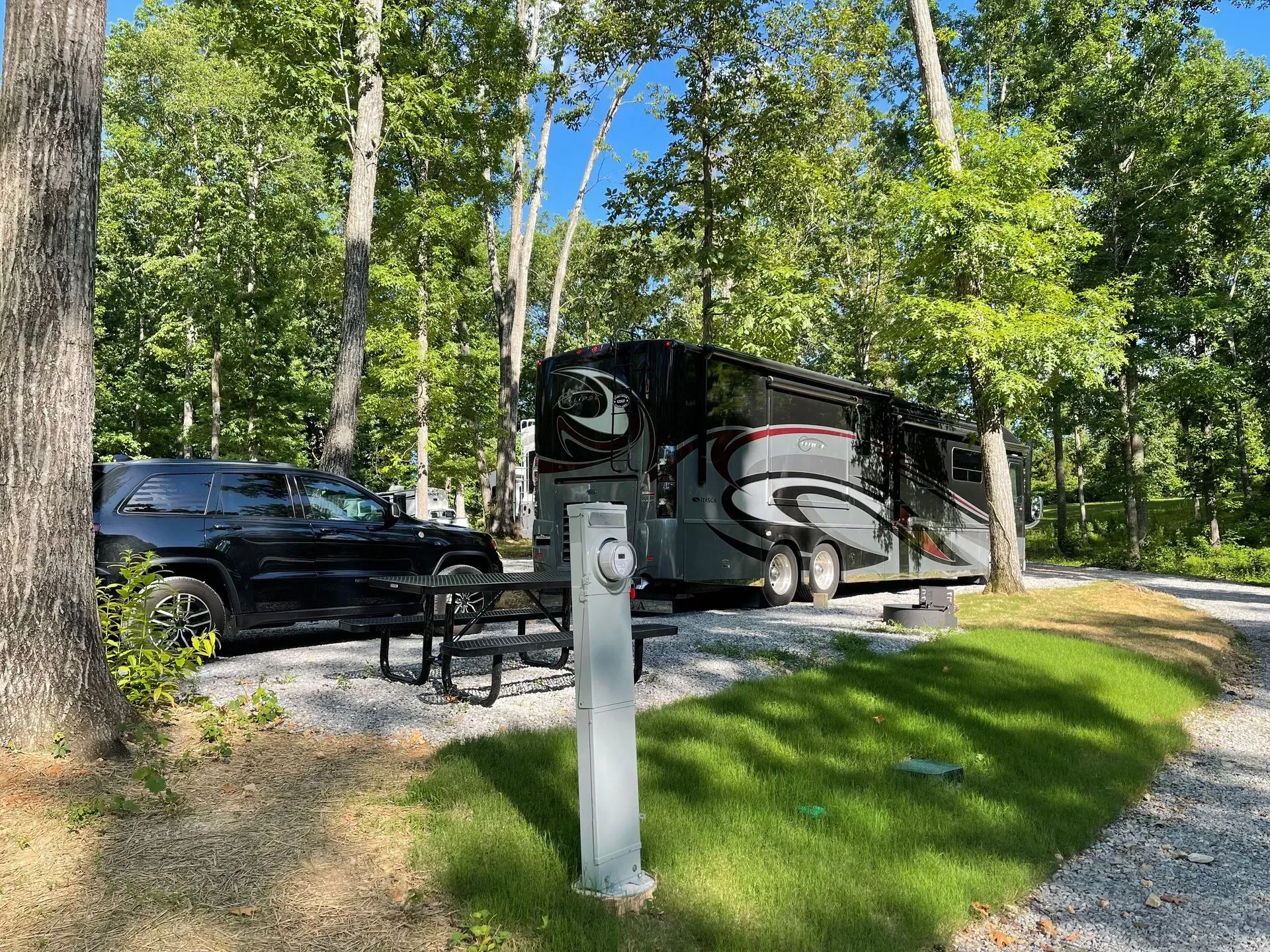 Black RV and SUV parked at a campsite with green grass and trees.