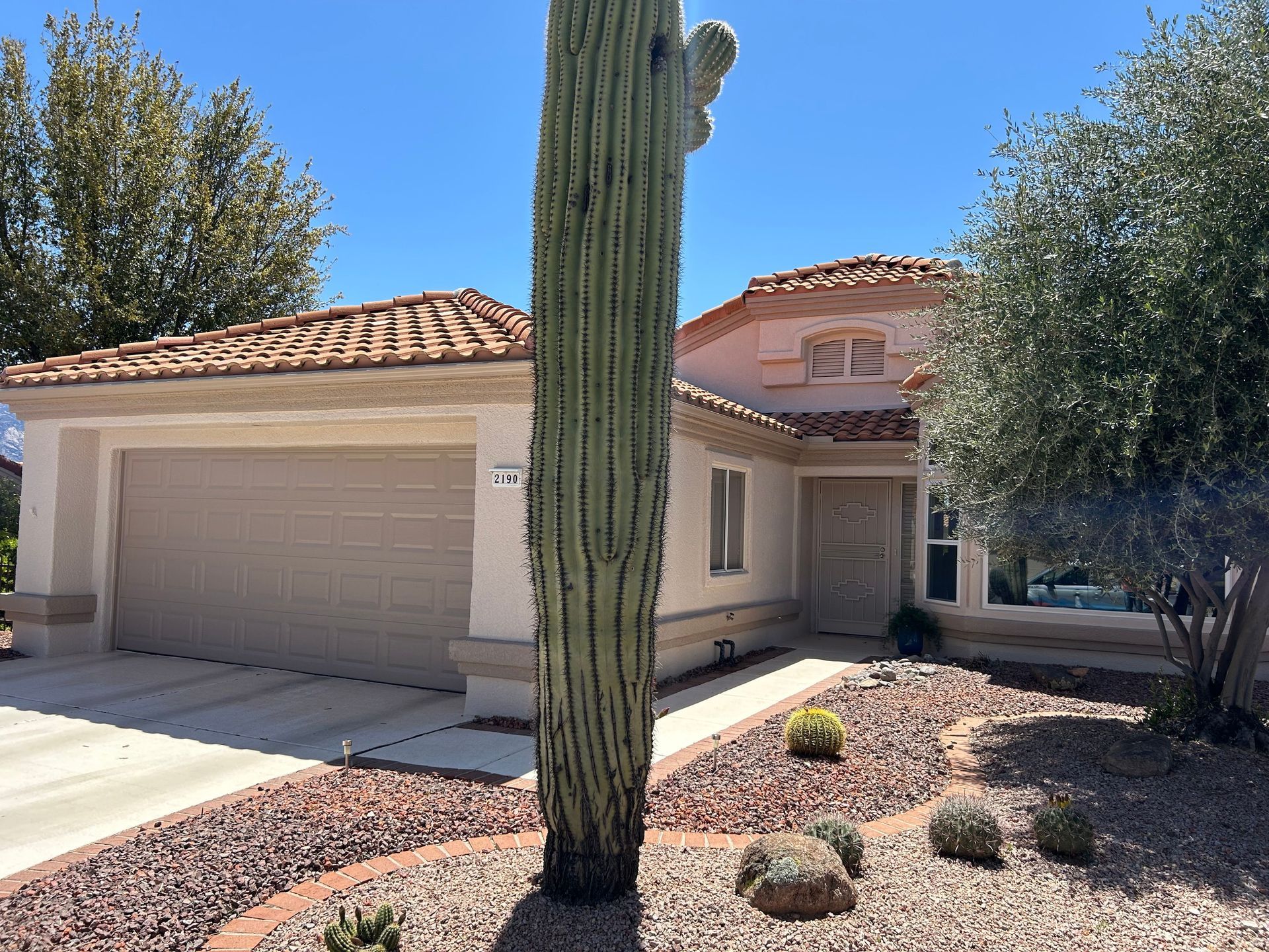 A light-colored home with a terracotta roof and a large saguaro cactus in the foreground. 