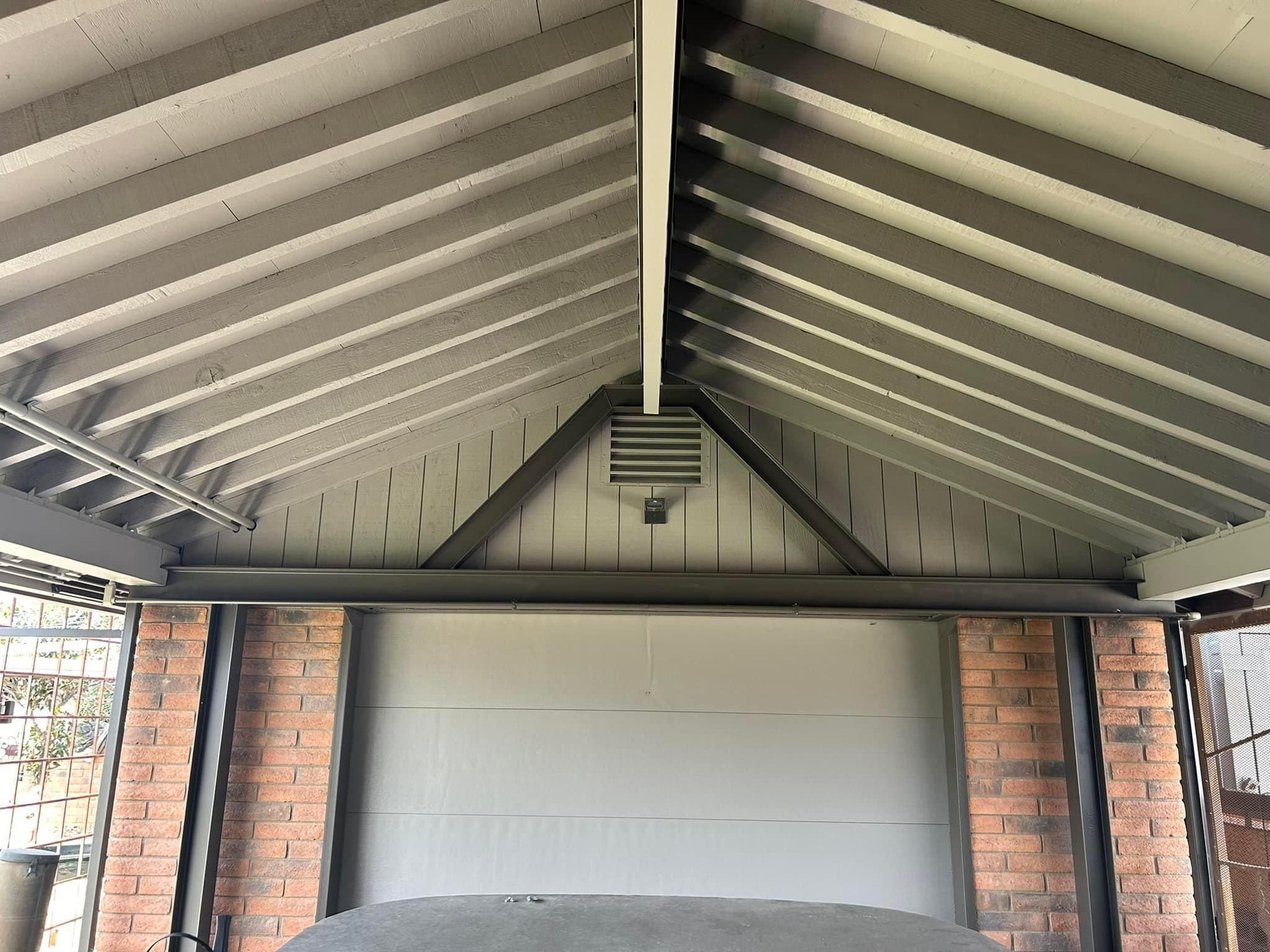 Garage interior with grey roof, brick columns, and a closed grey door. A vent is centered above the door.