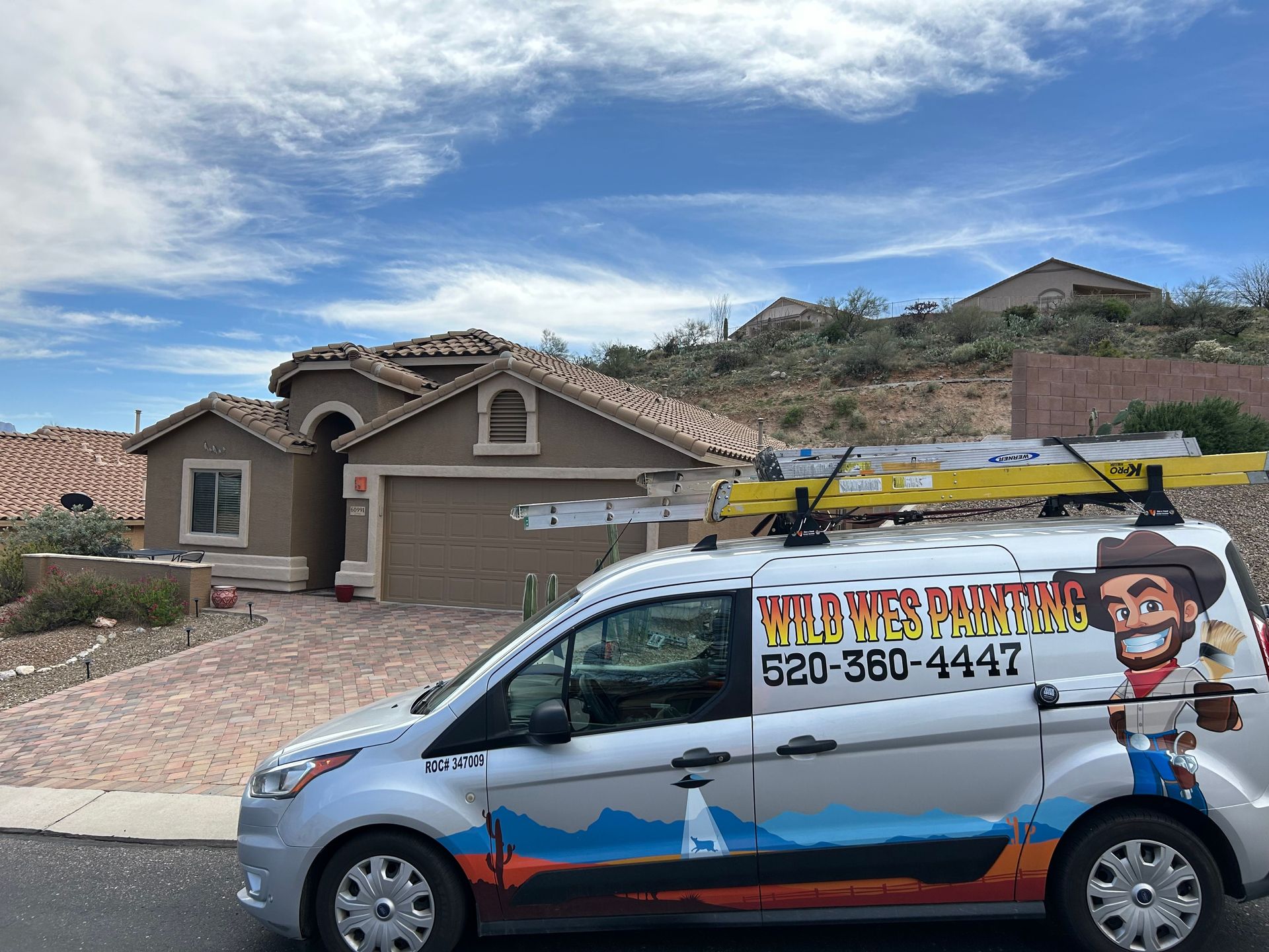 A service van with a cowboy logo parked in front of a beige house under a cloudy sky. The van has a ladder on its roof.