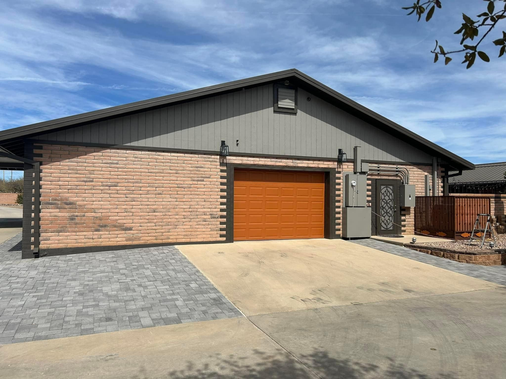 Garage with a brown garage door, gray brick facade, and a paved driveway under a blue sky.