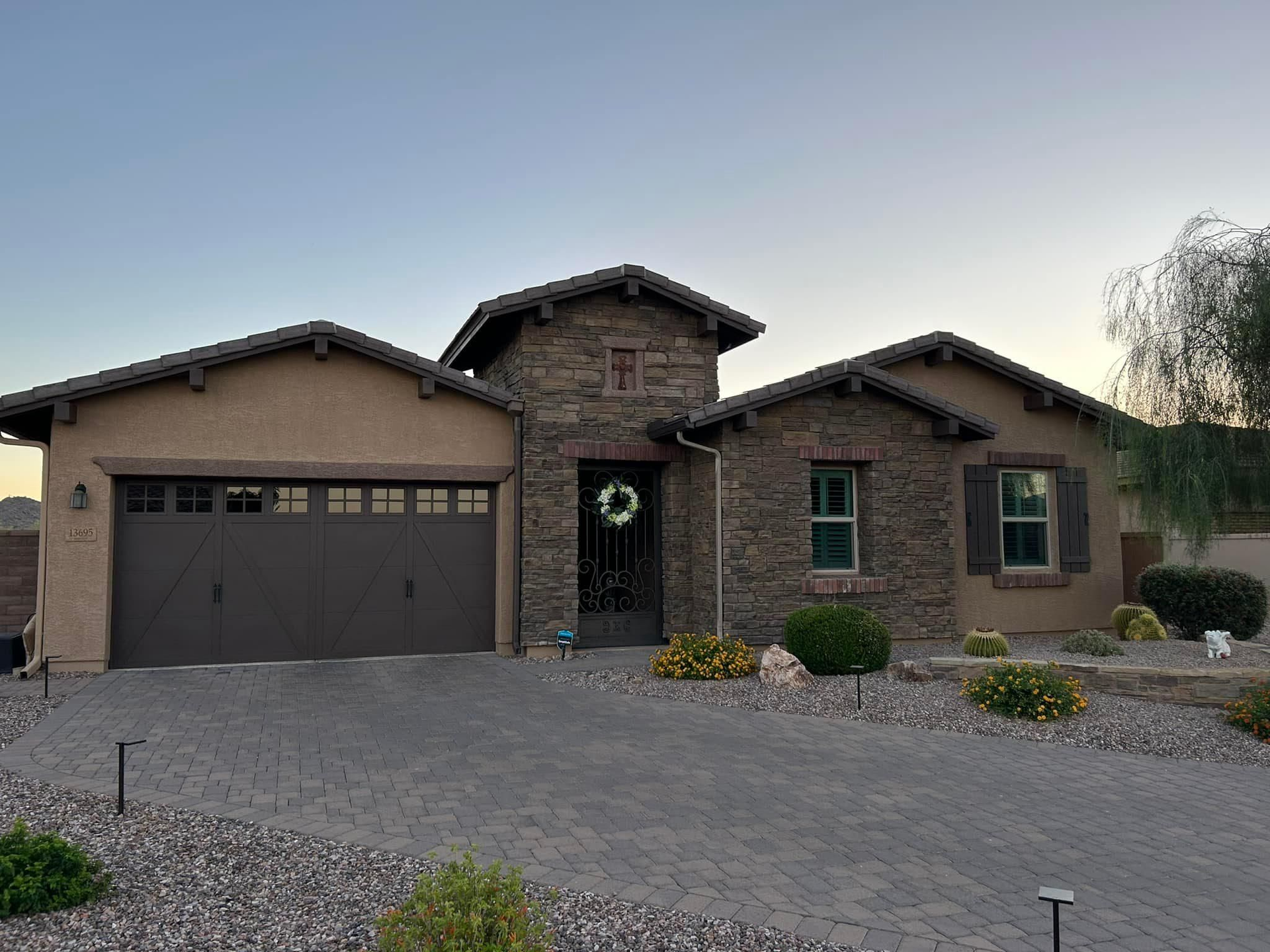 Single-story house with tan stucco and stone facade, a dark garage door, and paved driveway.