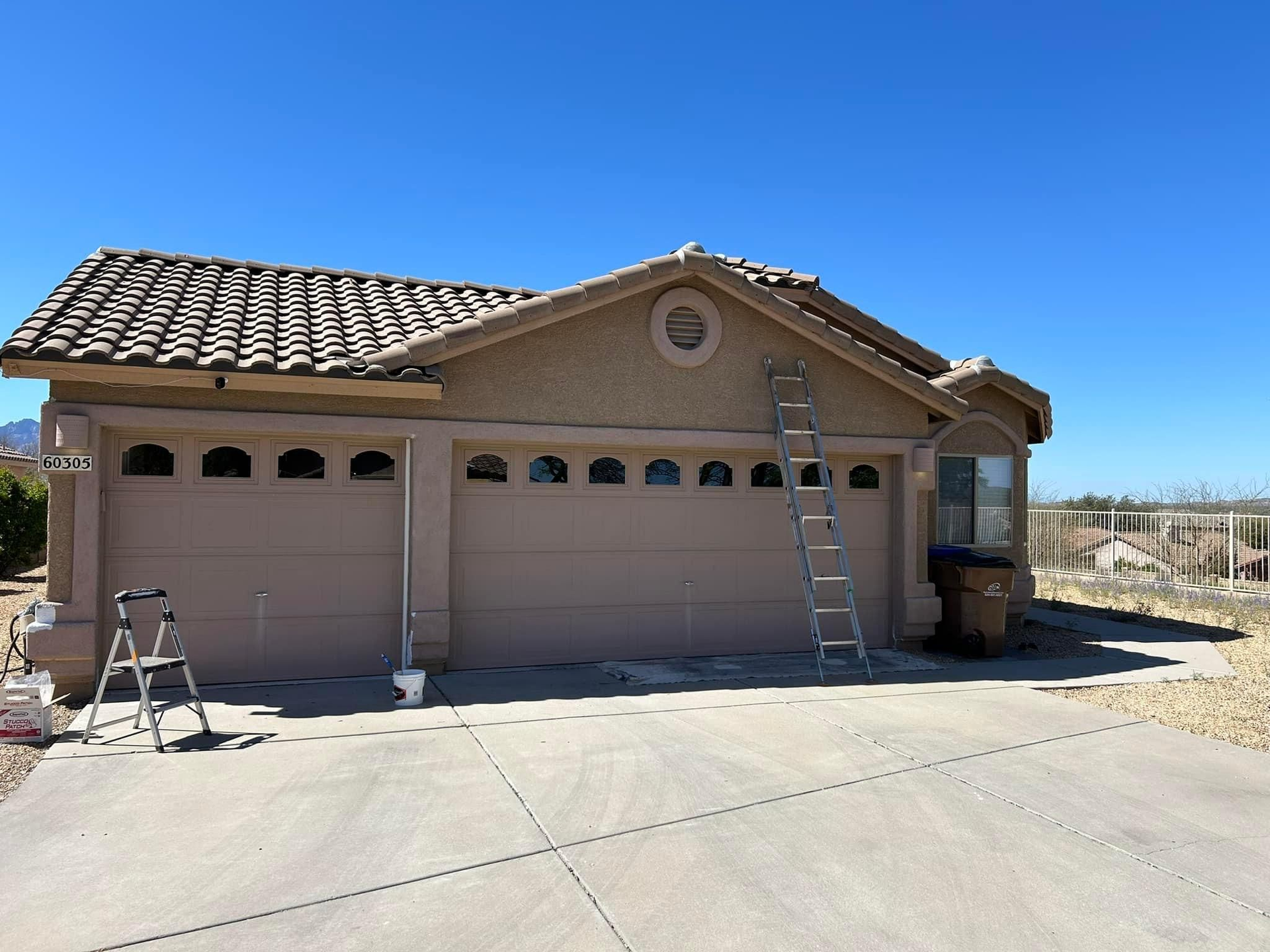 Tan house with a three-car garage. A ladder leans against the wall next to a garage door