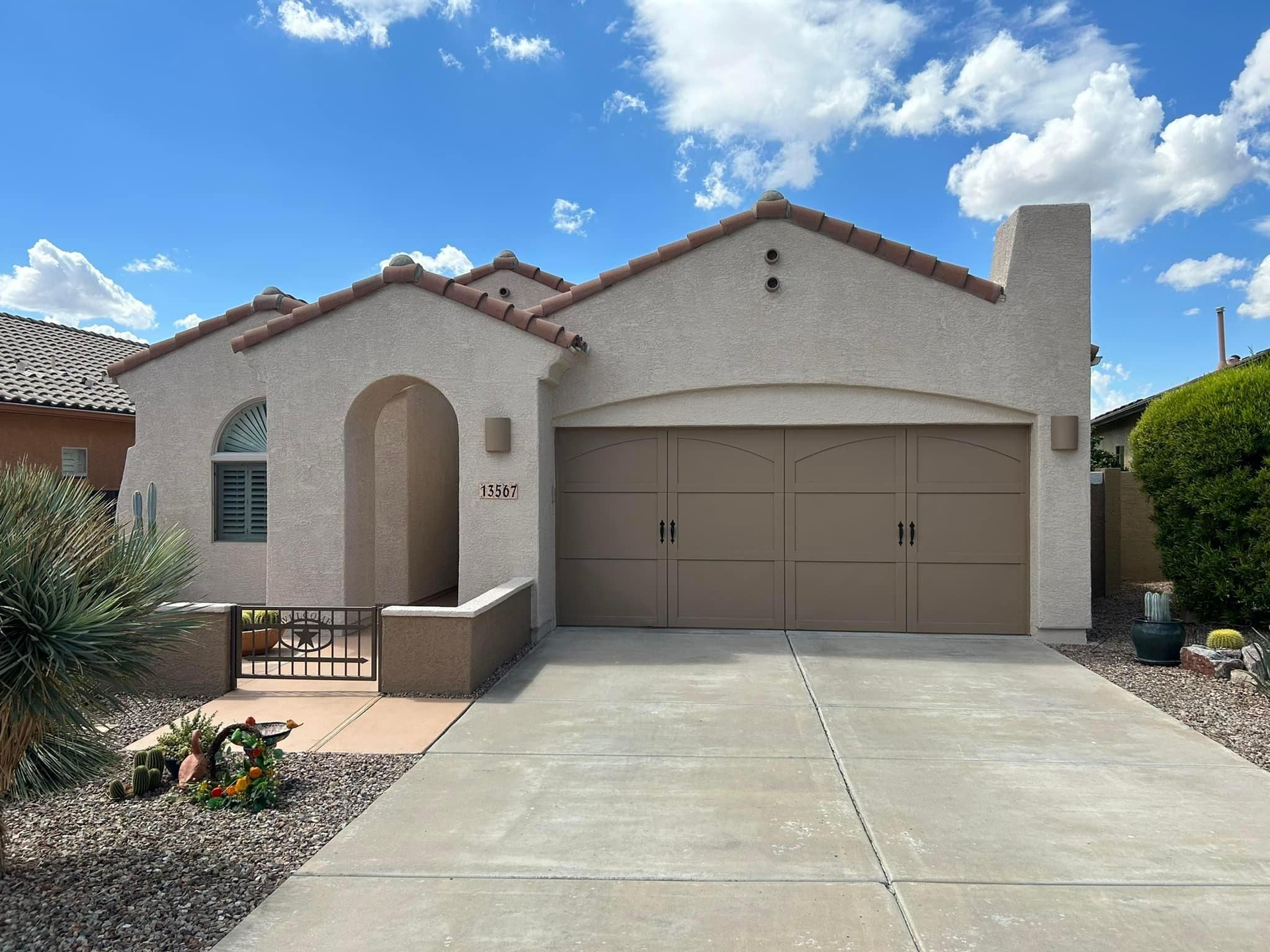 A tan stucco house with a brown garage door, a concrete driveway, and a blue sky.