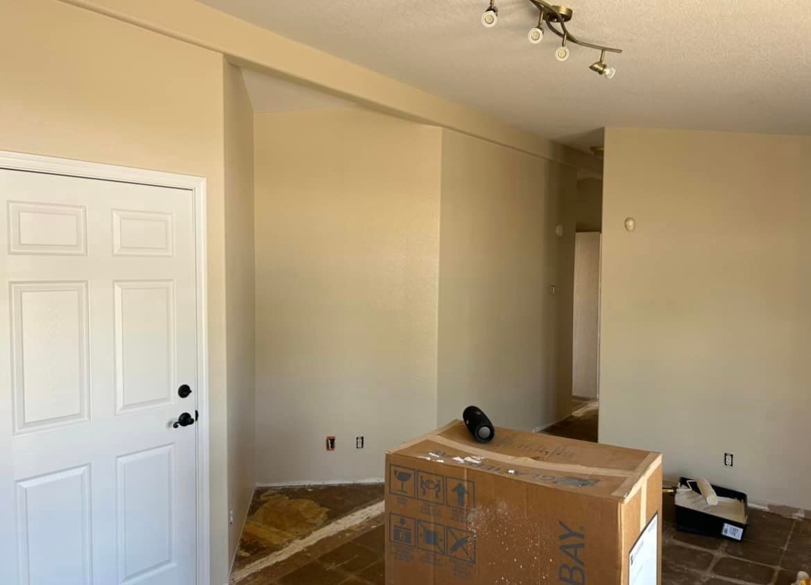 Interior room with an open doorway and a white front door. The walls are beige with a large cardboard box in the center.