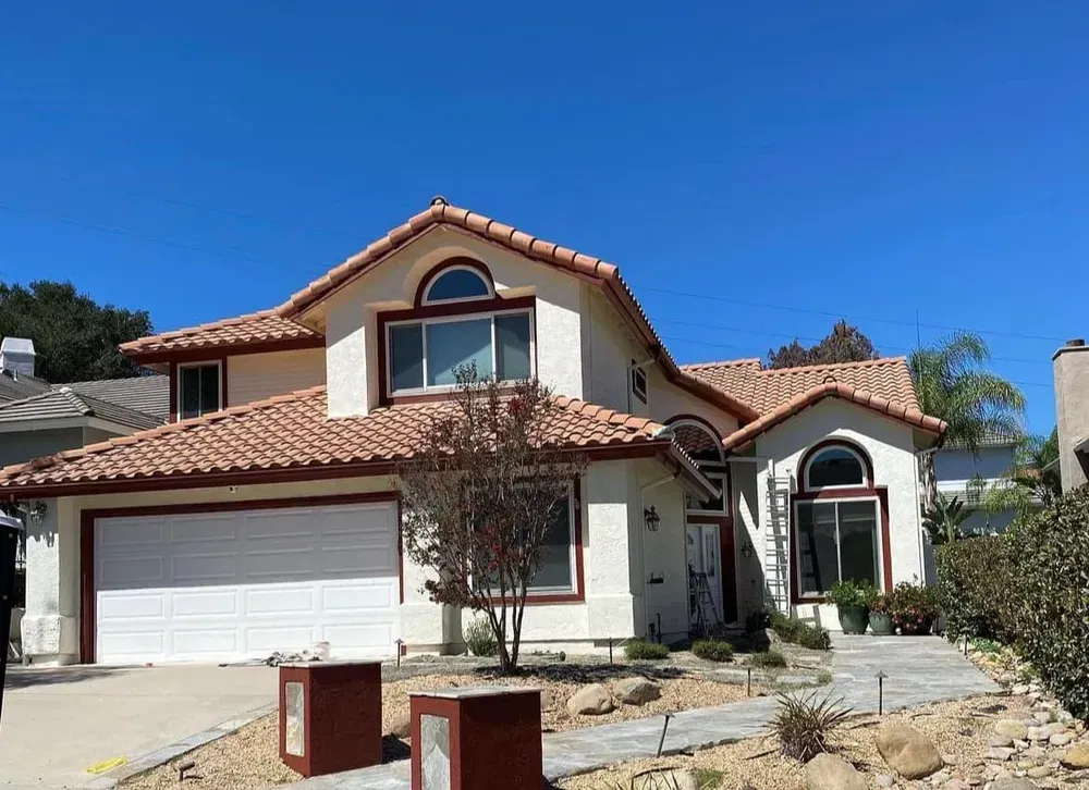 Two-story house with red-tiled roof and white walls, set against a clear blue sky. 
