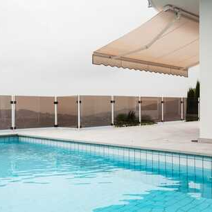 Outdoor awning extending out over pool paving, with pool in foreground, and looking out over pool fence at mountain terrain in background.