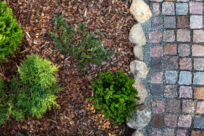 Green Shrubs and Brown Mulch Border a Cobblestone Walkway — Coastal Sand Soil & Mulch in Urangan, QLD